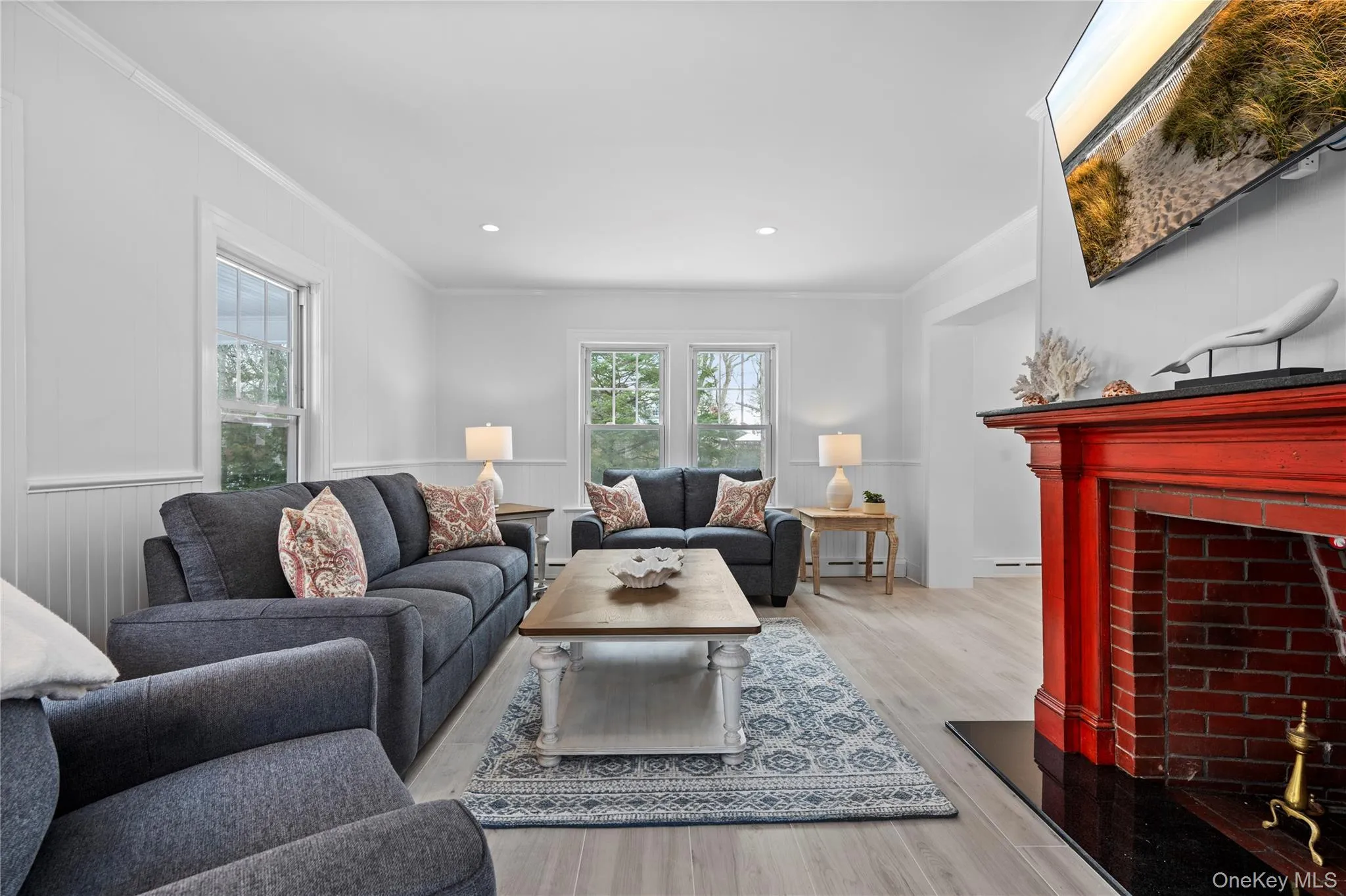 Living room featuring a brick fireplace, light wood-style flooring, a wainscoted wall, ornamental molding, and recessed lighting Living room featuring a brick fireplace, light wood-style flooring, a wainscoted wall, ornamental molding, and recessed lighting