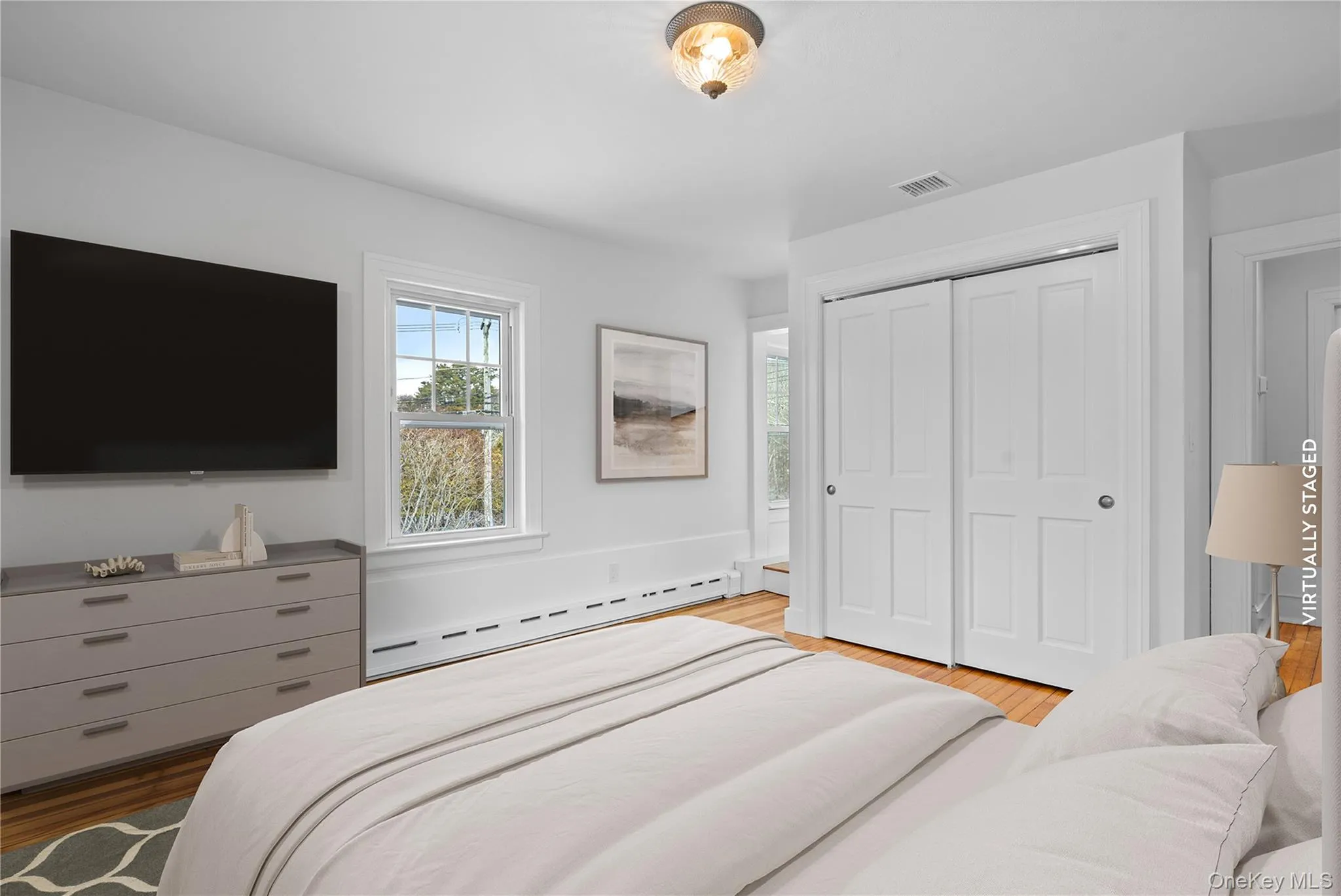 Bedroom with a baseboard heating unit, a closet, and light wood-type flooring Bedroom with a baseboard heating unit, a closet, and light wood-type flooring