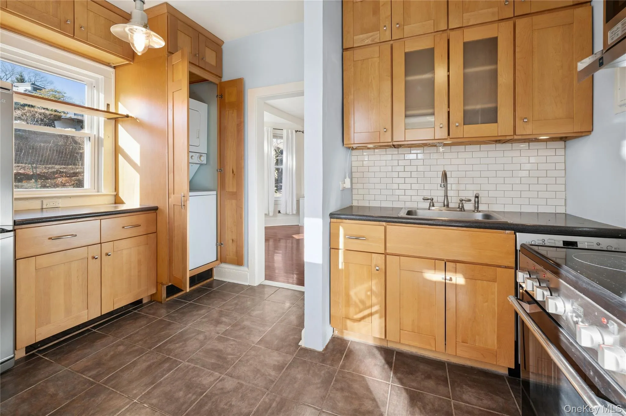 Kitchen featuring stainless steel range with electric cooktop, tasteful backsplash, glass insert cabinets, estacked washer and dryer, and light brown cabinets Kitchen featuring stainless steel range with electric cooktop, tasteful backsplash, glass insert cabinets, estacked washer and dryer, and light brown cabinets