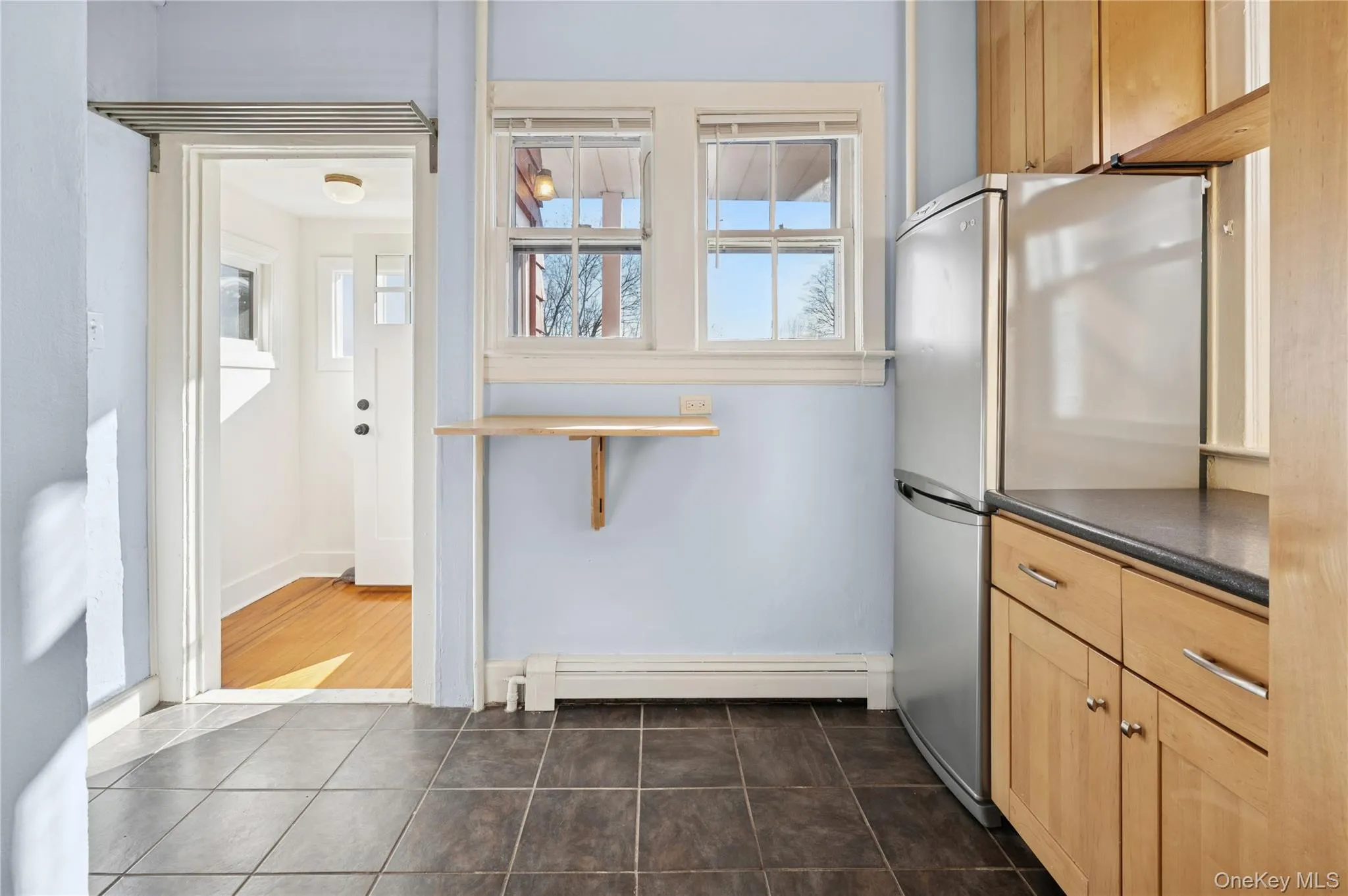 Kitchen with freestanding refrigerator, dark countertops, light brown cabinets, and healthy amount of natural light Kitchen with freestanding refrigerator, dark countertops, light brown cabinets, and healthy amount of natural light