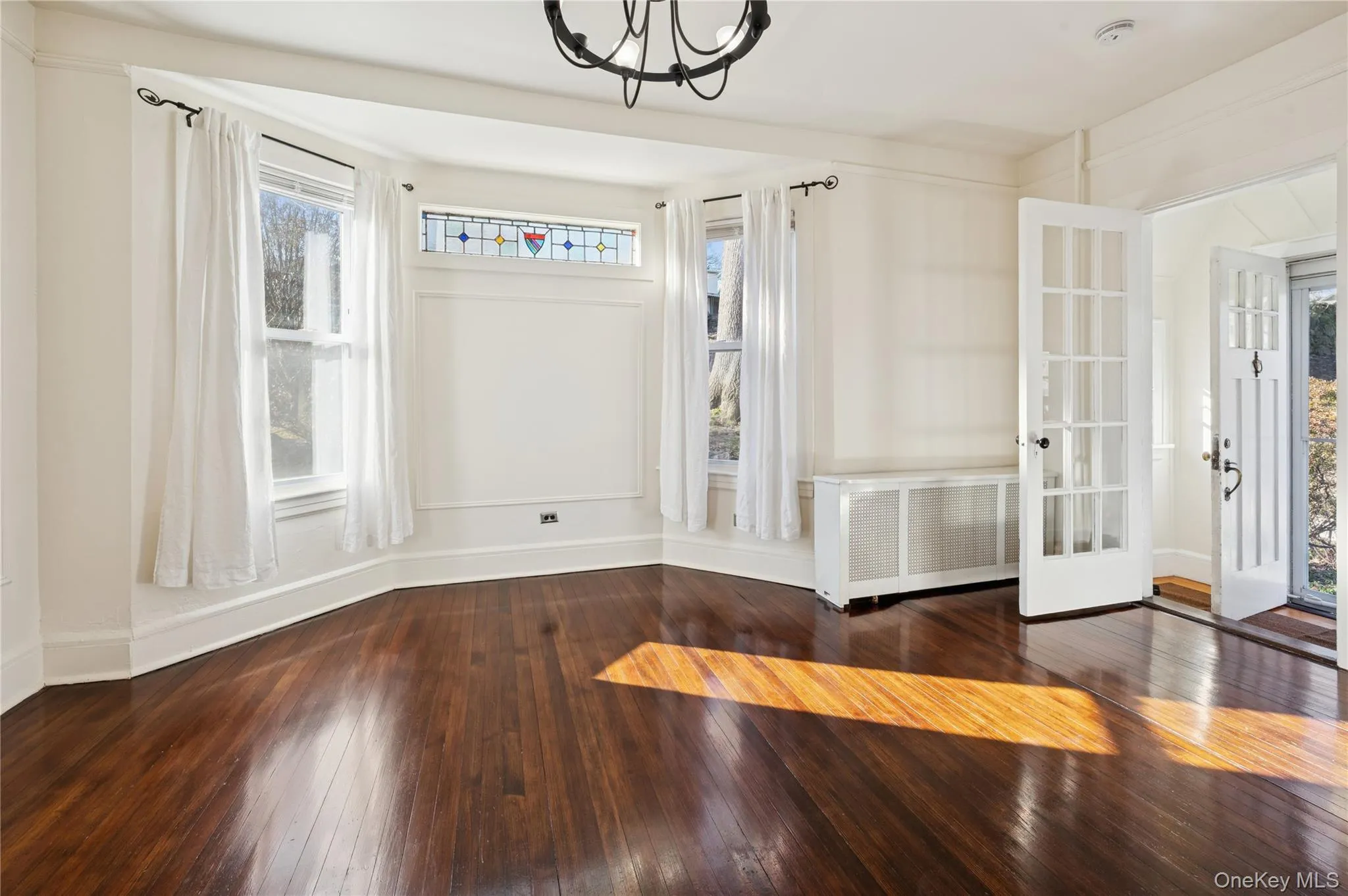 Unfurnished room with radiator heating unit, dark wood-style flooring, french doors, and a chandelier Unfurnished room with radiator heating unit, dark wood-style flooring, french doors, and a chandelier