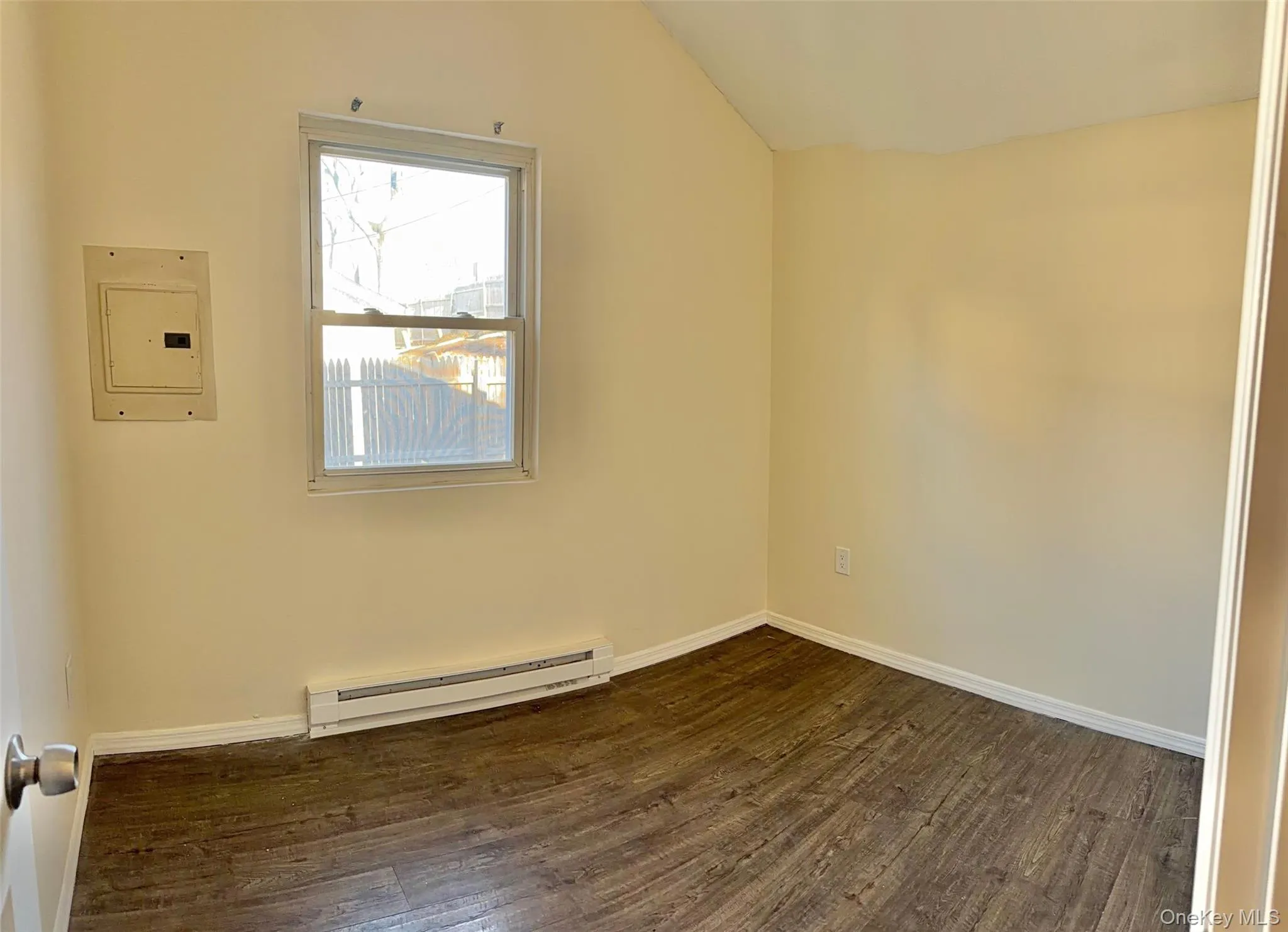 Empty room featuring a baseboard heating unit, dark wood-style flooring, electric panel, and lofted ceiling Empty room featuring a baseboard heating unit, dark wood-style flooring, electric panel, and lofted ceiling