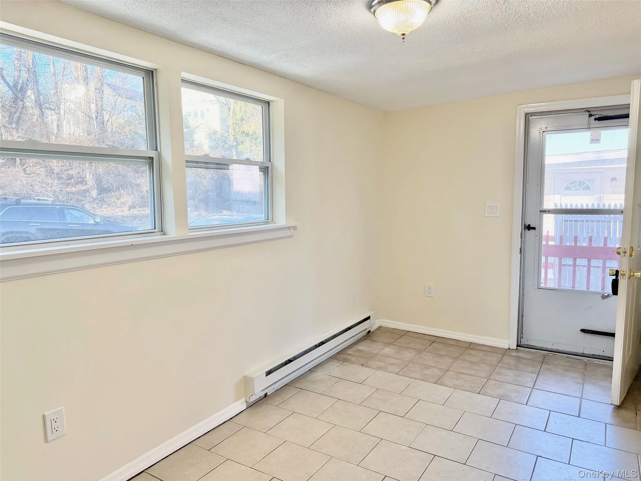 Unfurnished room featuring baseboard heating, a textured ceiling, plenty of natural light, and light tile patterned floors Unfurnished room featuring baseboard heating, a textured ceiling, plenty of natural light, and light tile patterned floors
