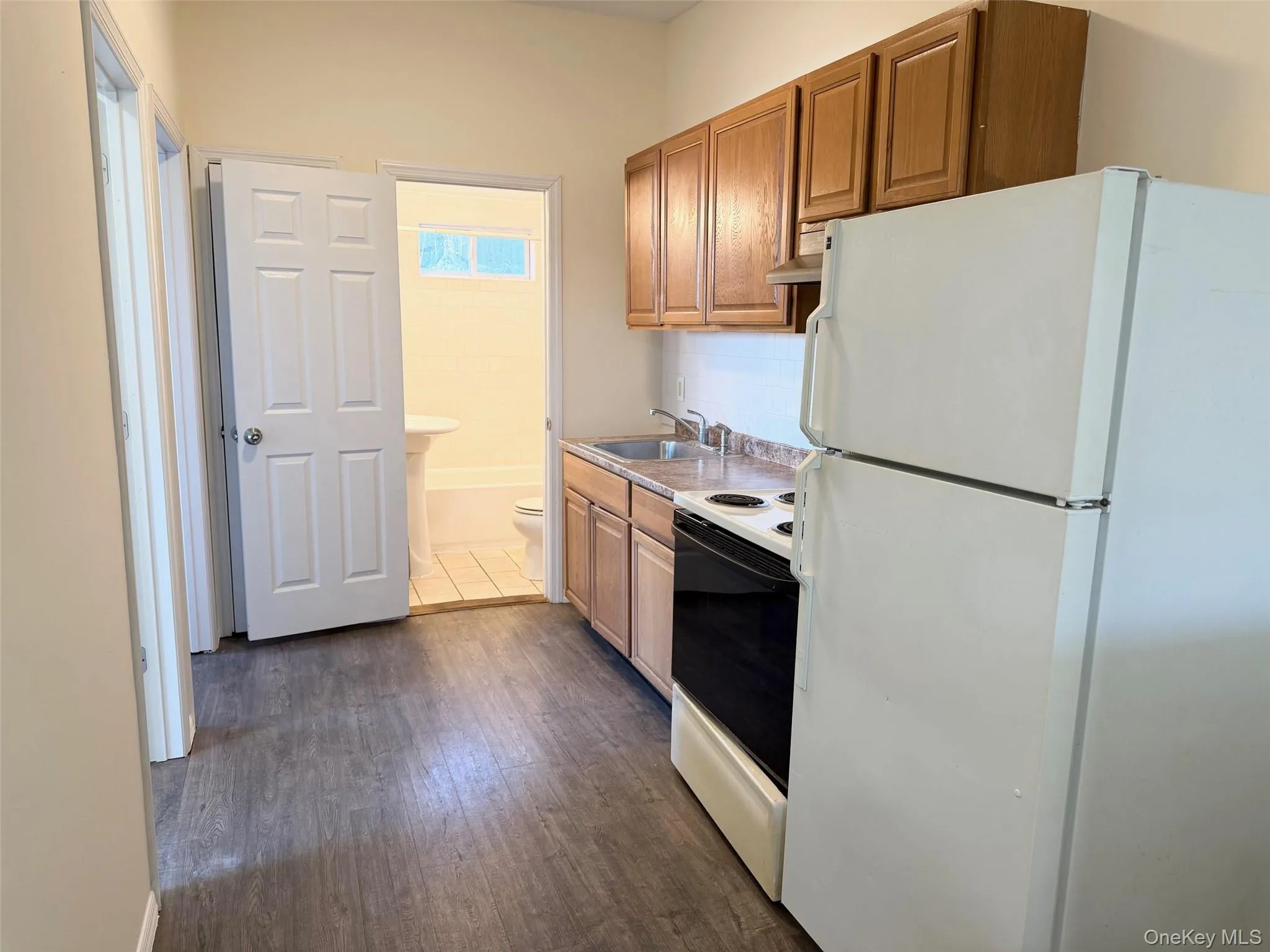 Kitchen featuring white appliances, brown cabinets, dark wood-style flooring, light countertops, and exhaust hood Kitchen featuring white appliances, brown cabinets, dark wood-style flooring, light countertops, and exhaust hood