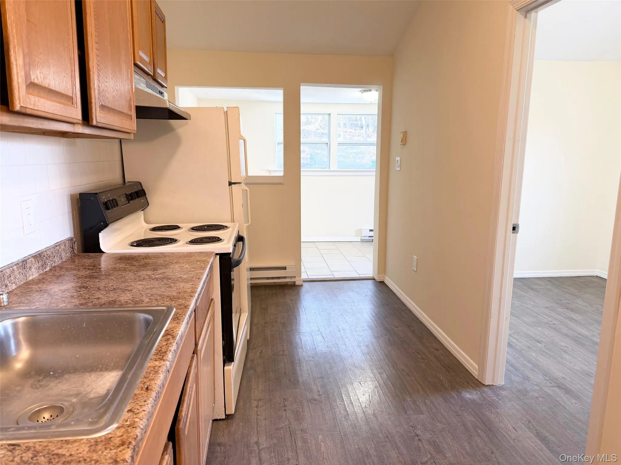 Kitchen with white range with electric cooktop, dark wood-type flooring, under cabinet range hood, a baseboard heating unit, and tasteful backsplash Kitchen with white range with electric cooktop, dark wood-type flooring, under cabinet range hood, a baseboard heating unit, and tasteful backsplash