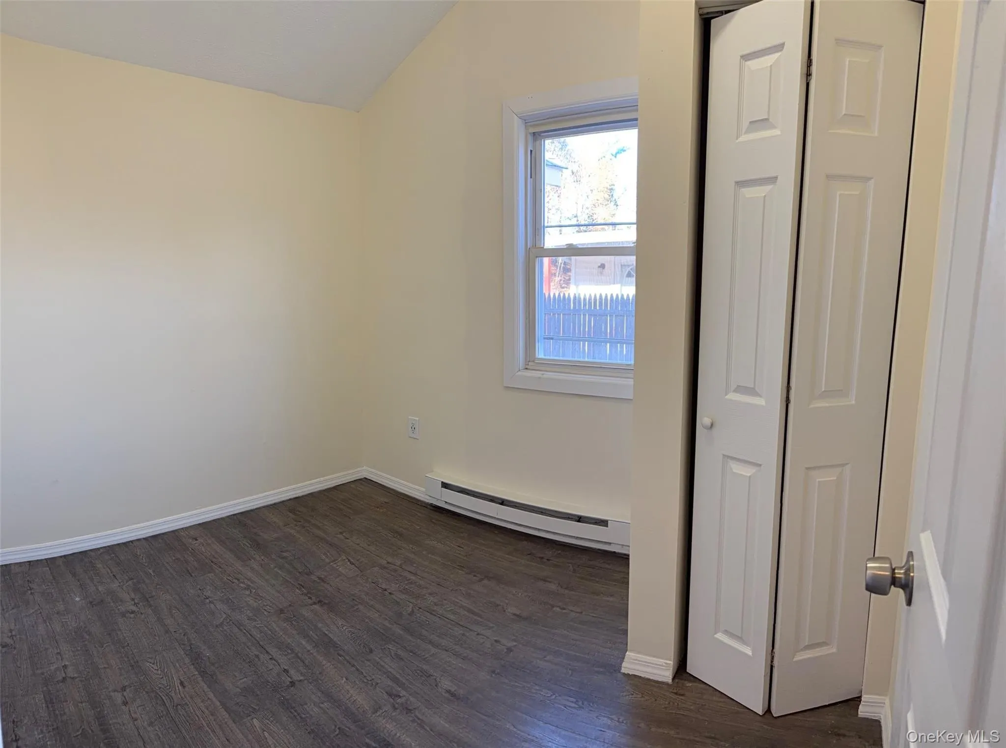 Unfurnished bedroom with lofted ceiling, dark wood-style flooring, baseboard heating, and a closet Unfurnished bedroom with lofted ceiling, dark wood-style flooring, baseboard heating, and a closet