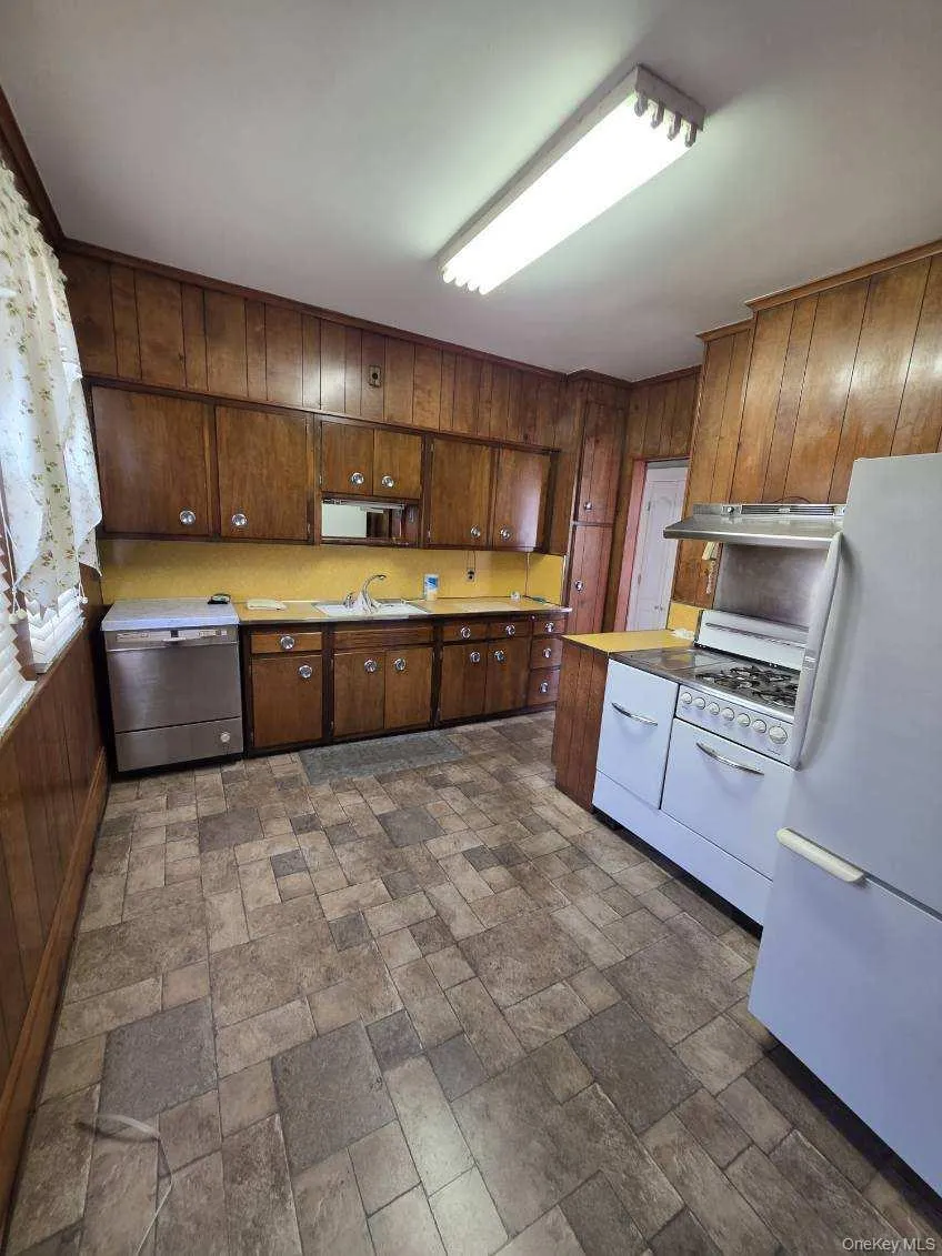 Kitchen with white appliances, wooden walls, light countertops, stone finish floors, and range hood Kitchen with white appliances, wooden walls, light countertops, stone finish floors, and range hood