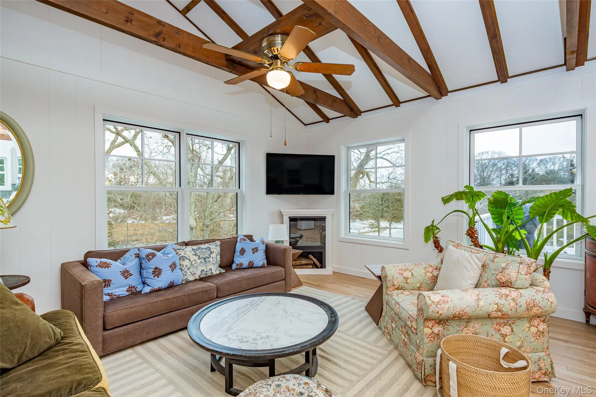 Living room featuring healthy amount of natural light, a glass covered fireplace, ceiling fan, and light wood-type flooring Living room featuring healthy amount of natural light, a glass covered fireplace, ceiling fan, and light wood-type flooring