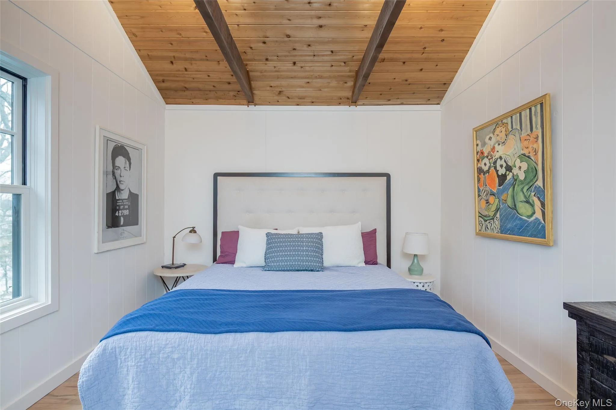 Bedroom featuring vaulted ceiling, wood walls, light wood-style floors, and multiple windows Bedroom featuring vaulted ceiling, wood walls, light wood-style floors, and multiple windows