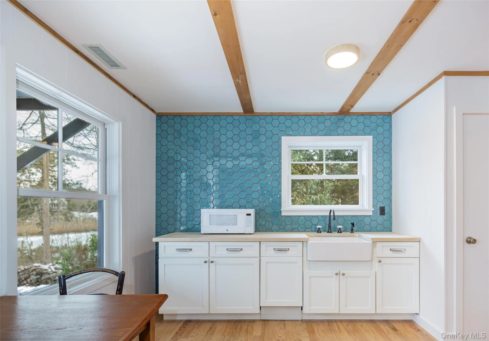 Kitchen with white cabinets, white microwave, light wood finished floors, beam ceiling, and crown molding Kitchen with white cabinets, white microwave, light wood finished floors, beam ceiling, and crown molding