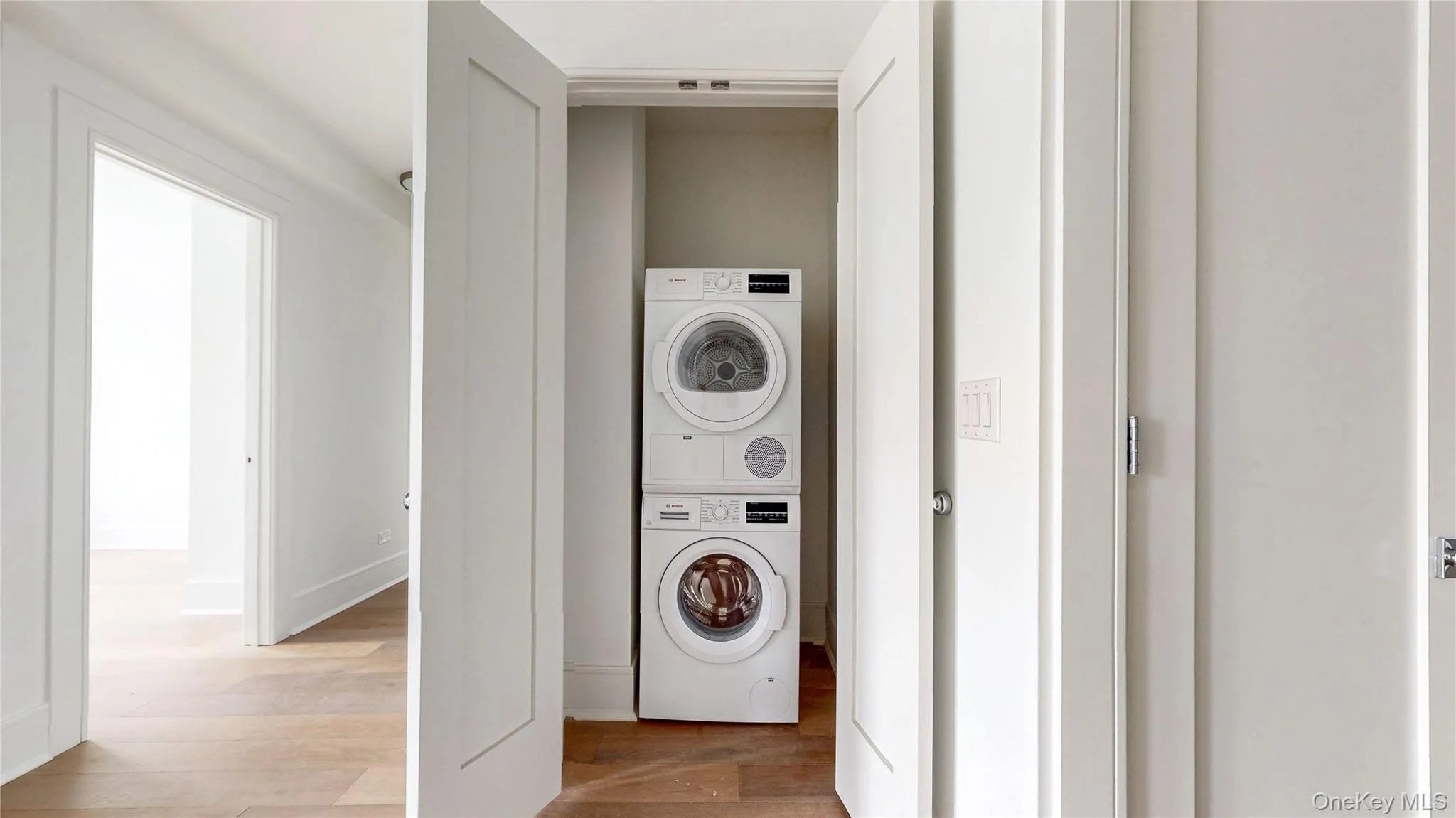 Laundry area featuring stacked washer / drying machine and wood finished floors Laundry area featuring stacked washer / drying machine and wood finished floors