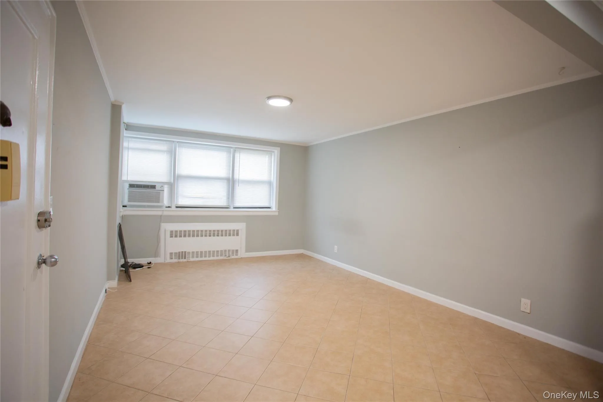Unfurnished room with radiator heating unit, crown molding, cooling unit, and light tile patterned floors Unfurnished room with radiator heating unit, crown molding, cooling unit, and light tile patterned floors
