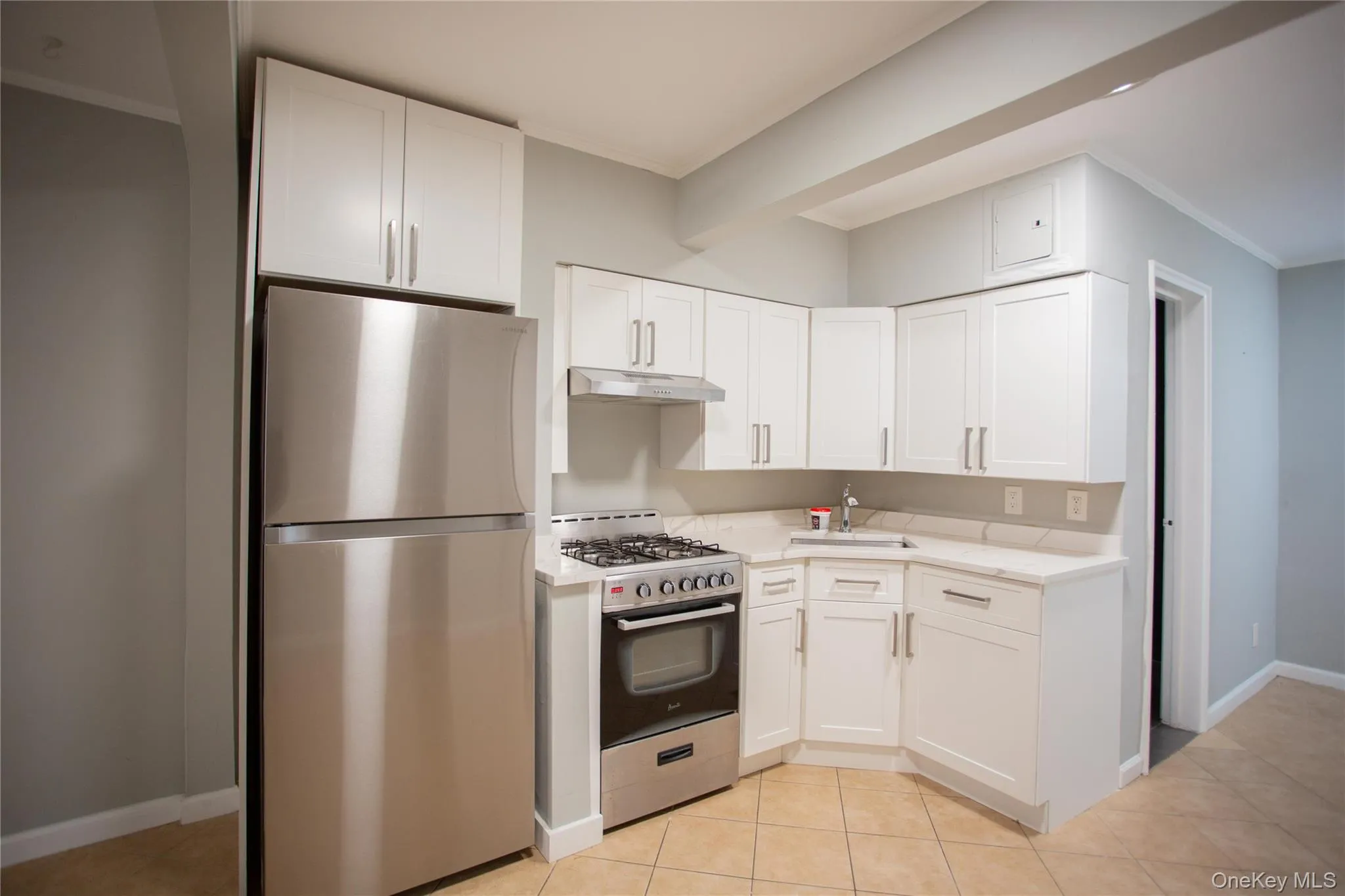Kitchen with crown molding, appliances with stainless steel finishes, white cabinetry, light tile patterned flooring, and under cabinet range hood Kitchen with crown molding, appliances with stainless steel finishes, white cabinetry, light tile patterned flooring, and under cabinet range hood