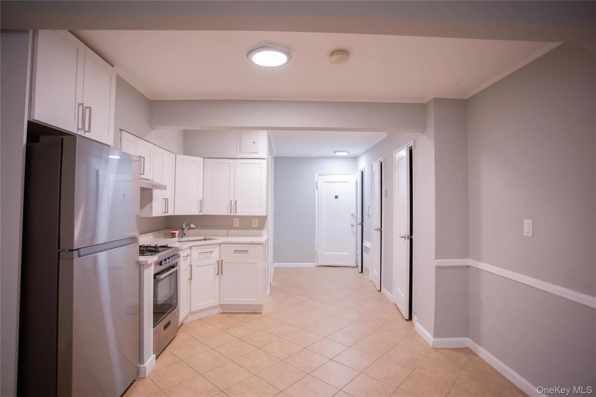 Kitchen featuring stainless steel appliances, light countertops, white cabinetry, crown molding, and light tile patterned flooring Kitchen featuring stainless steel appliances, light countertops, white cabinetry, crown molding, and light tile patterned flooring