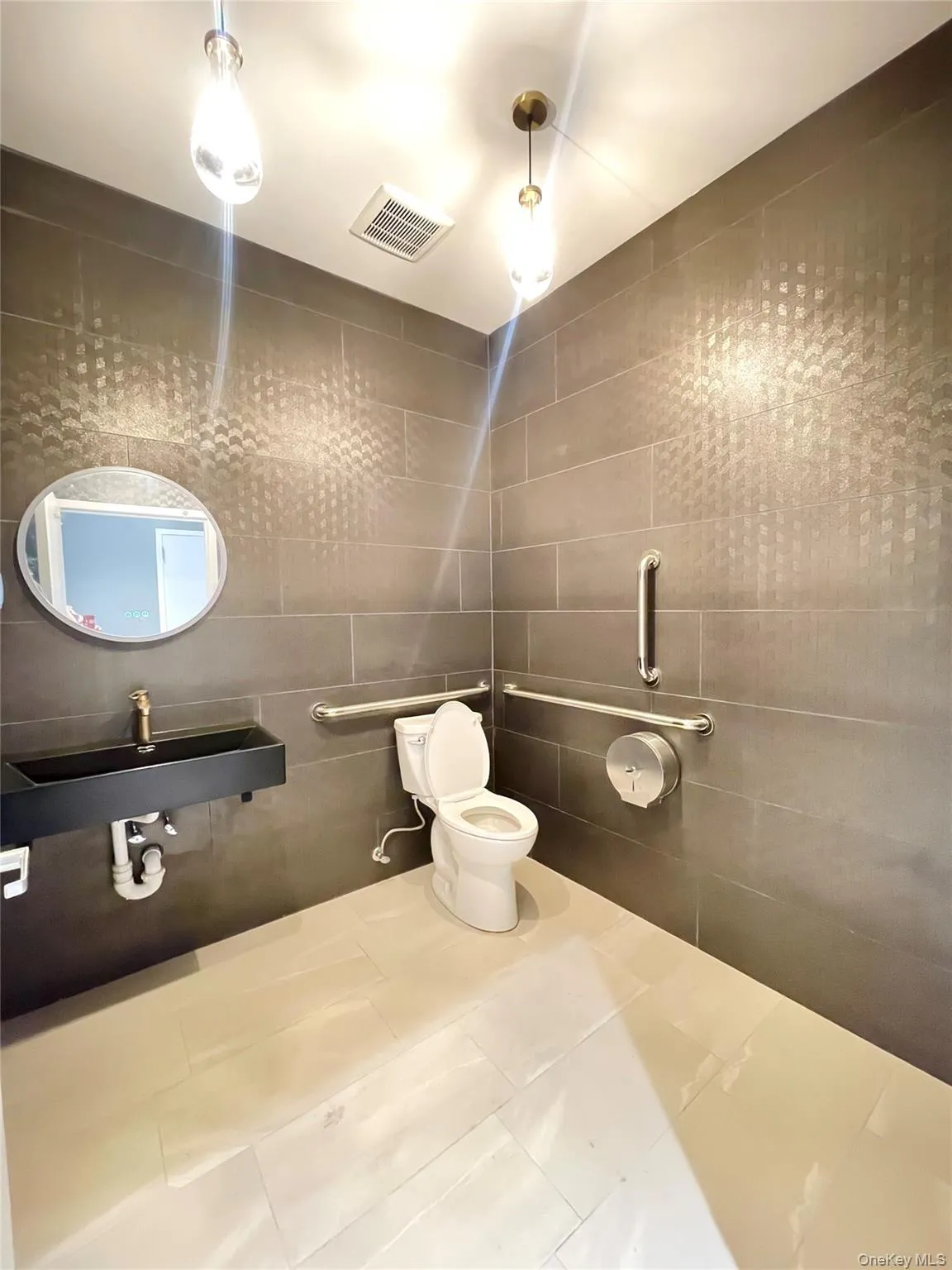 Bathroom featuring tile patterned floors, toilet, a sink, visible vents, and tile walls Bathroom featuring tile patterned floors, toilet, a sink, visible vents, and tile walls