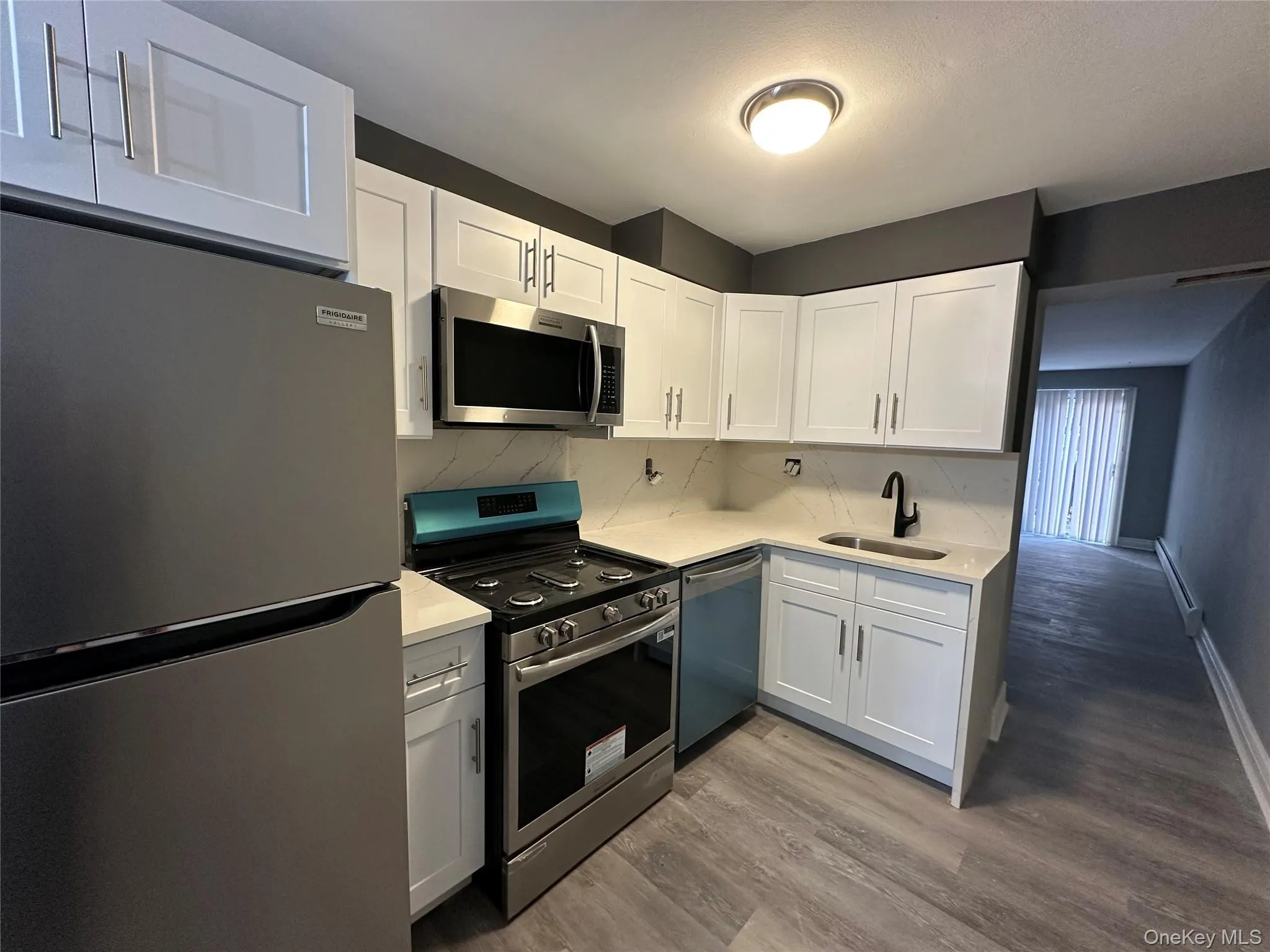 Kitchen featuring stainless steel appliances, white cabinets, light stone countertops, baseboard heating, and backsplash Kitchen featuring stainless steel appliances, white cabinets, light stone countertops, baseboard heating, and backsplash