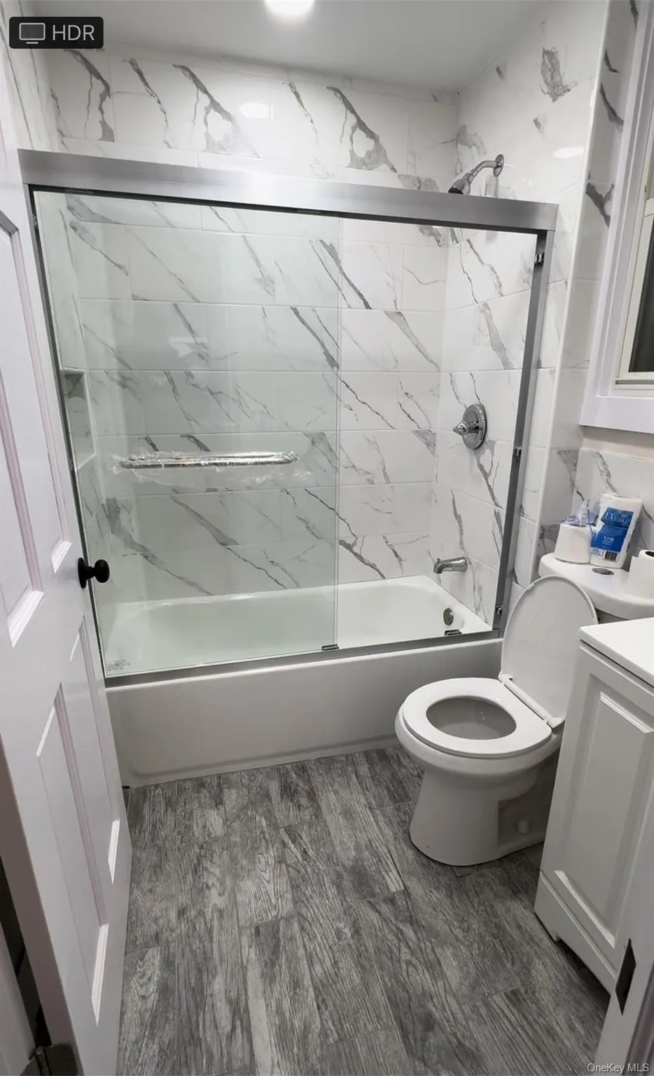 Full bathroom featuring vanity, shower / bath combination with glass door, and light wood-type flooring Full bathroom featuring vanity, shower / bath combination with glass door, and light wood-type flooring