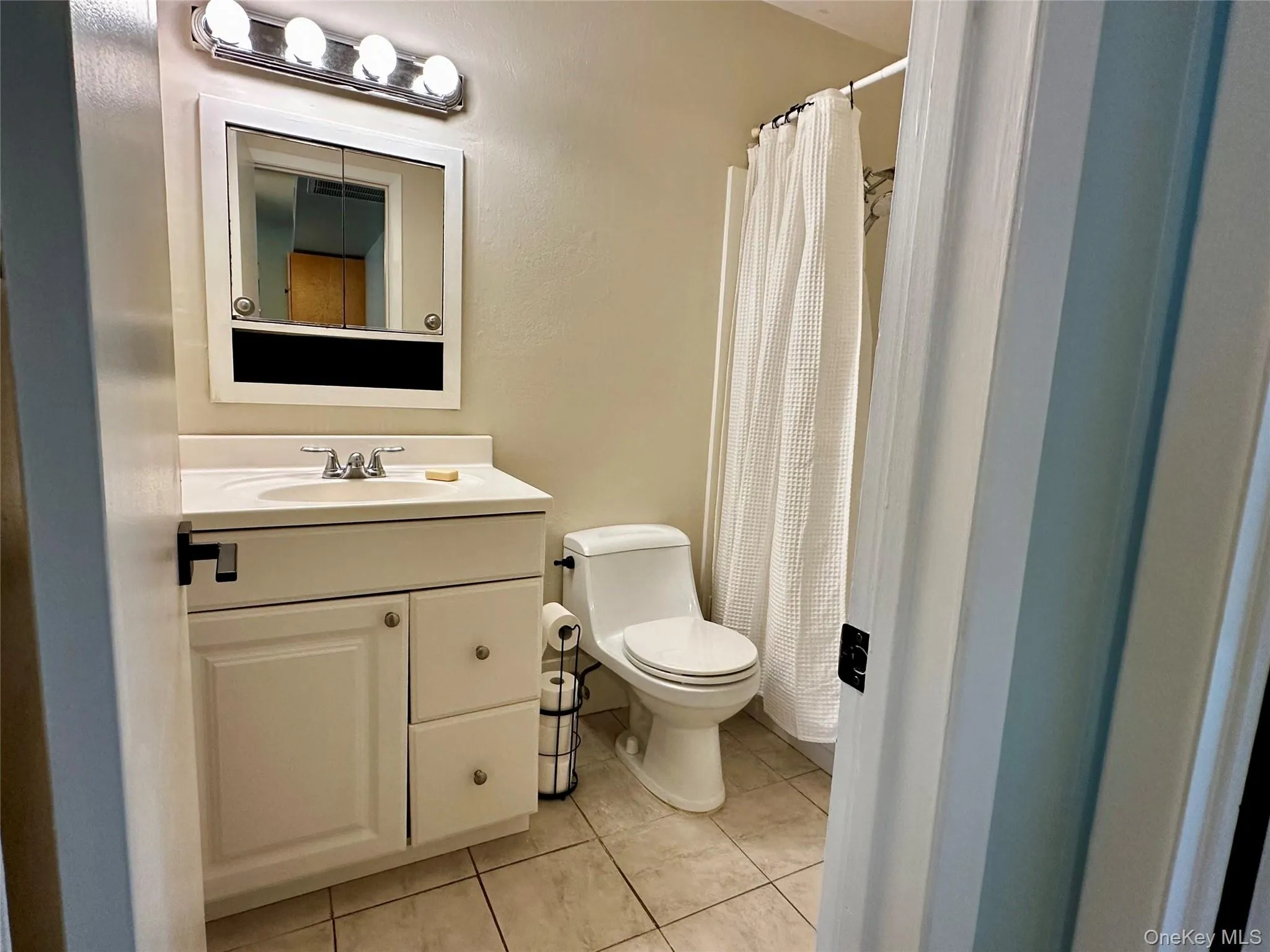 Bathroom featuring a shower with shower curtain, vanity, and light tile floors Bathroom featuring a shower with shower curtain, vanity, and light tile floors