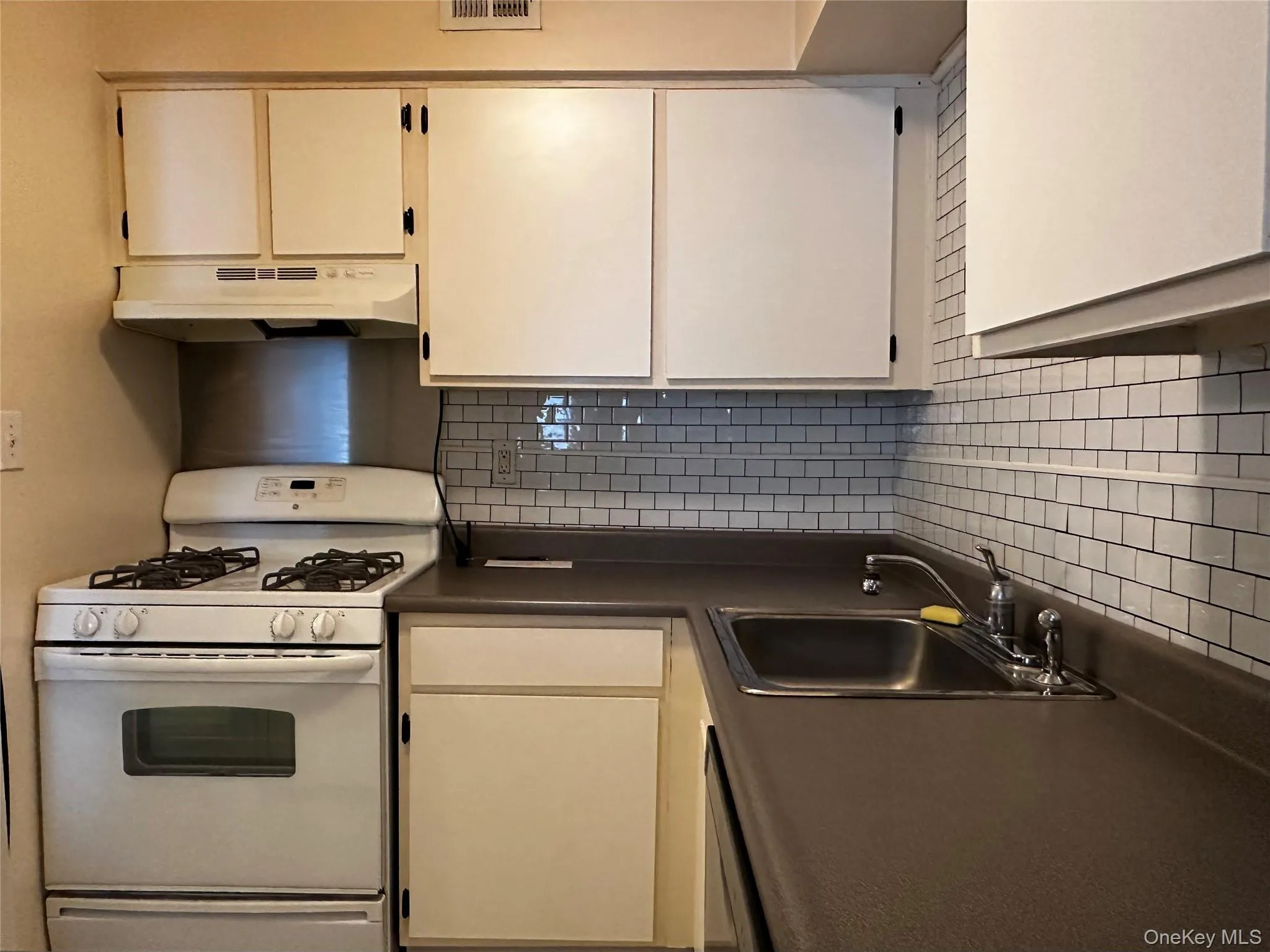 Kitchen with white gas range, tile backsplash, under cabinet range hood, and dark countertops Kitchen with white gas range, tile backsplash, under cabinet range hood, and dark countertops