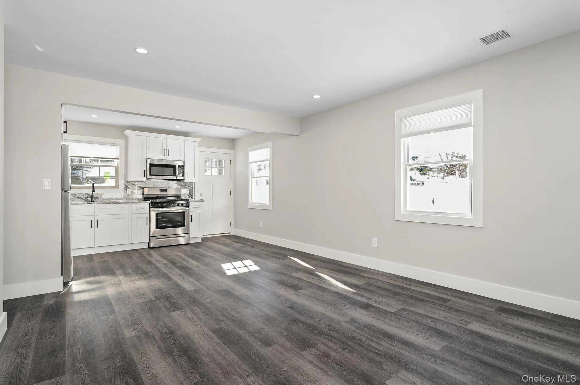 Kitchen with white cabinets, stainless steel appliances, dark wood-style flooring, recessed lighting, and light stone countertops Kitchen with white cabinets, stainless steel appliances, dark wood-style flooring, recessed lighting, and light stone countertops