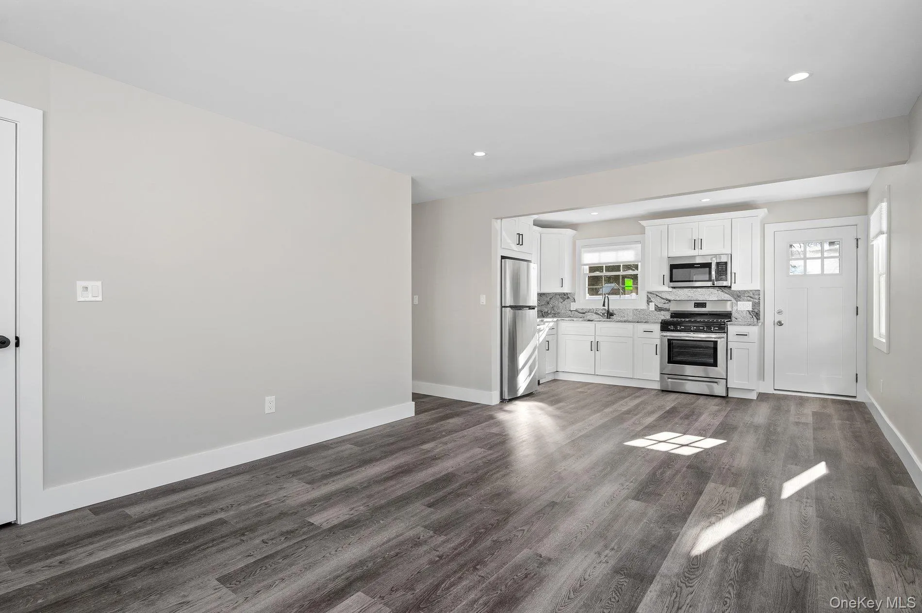 Kitchen featuring stainless steel appliances, white cabinets, dark wood-style flooring, tasteful backsplash, and recessed lighting Kitchen featuring stainless steel appliances, white cabinets, dark wood-style flooring, tasteful backsplash, and recessed lighting