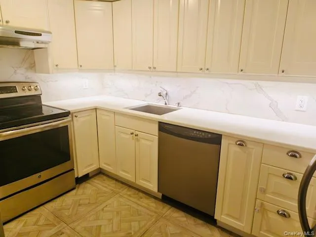 Kitchen featuring appliances with stainless steel finishes, light countertops, under cabinet range hood, and backsplash Kitchen featuring appliances with stainless steel finishes, light countertops, under cabinet range hood, and backsplash