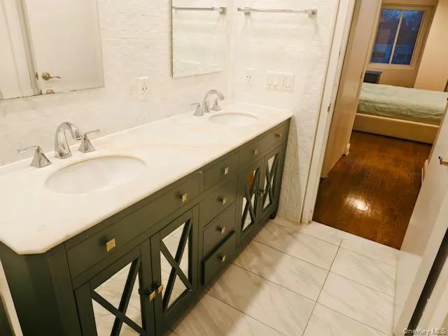 Bathroom featuring double vanity, connected bathroom, and tile walls Bathroom featuring double vanity, connected bathroom, and tile walls