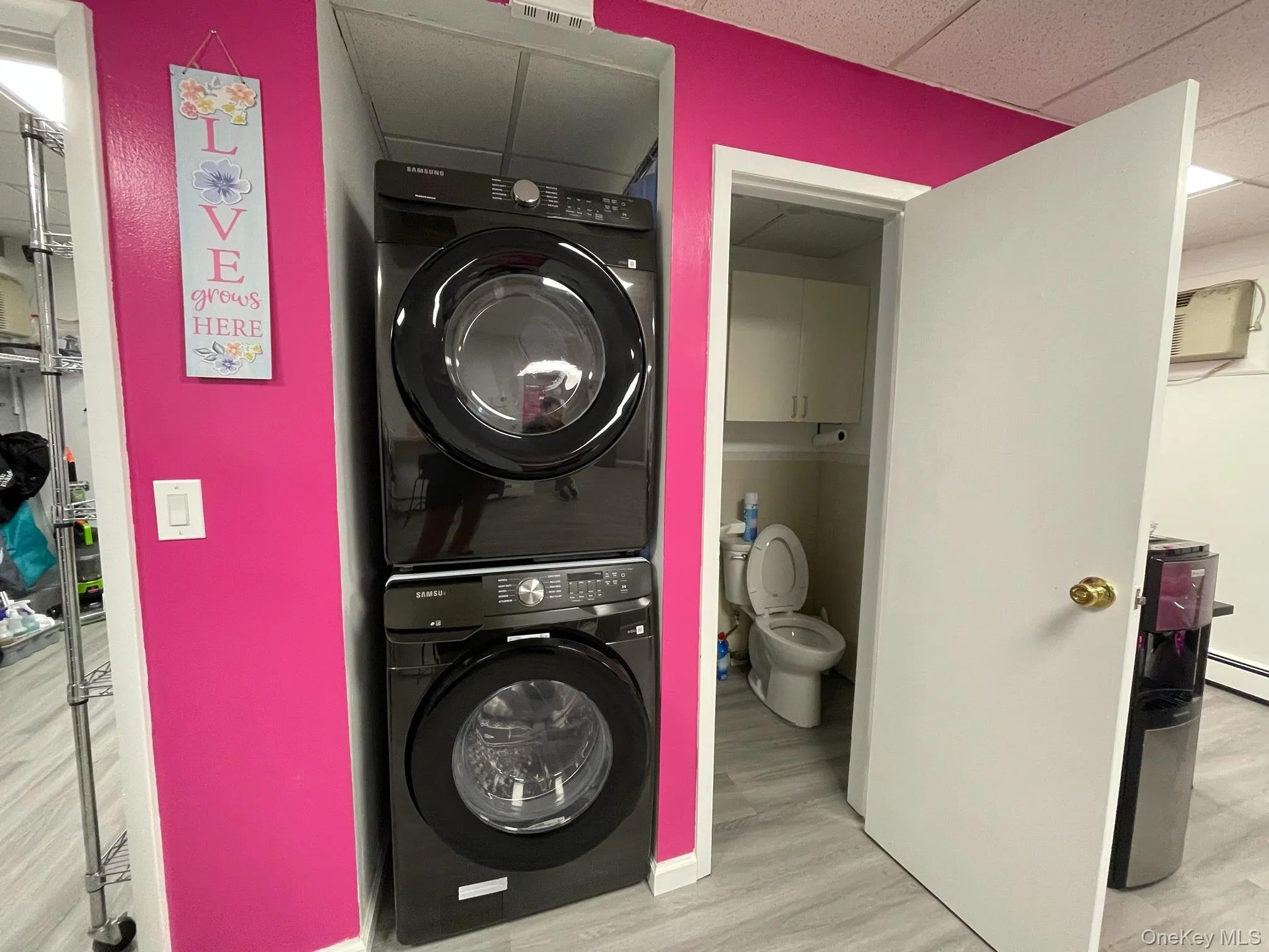 Washroom with a paneled ceiling, stacked washing machine and dryer, and light wood-style flooring Washroom with a paneled ceiling, stacked washing machine and dryer, and light wood-style flooring