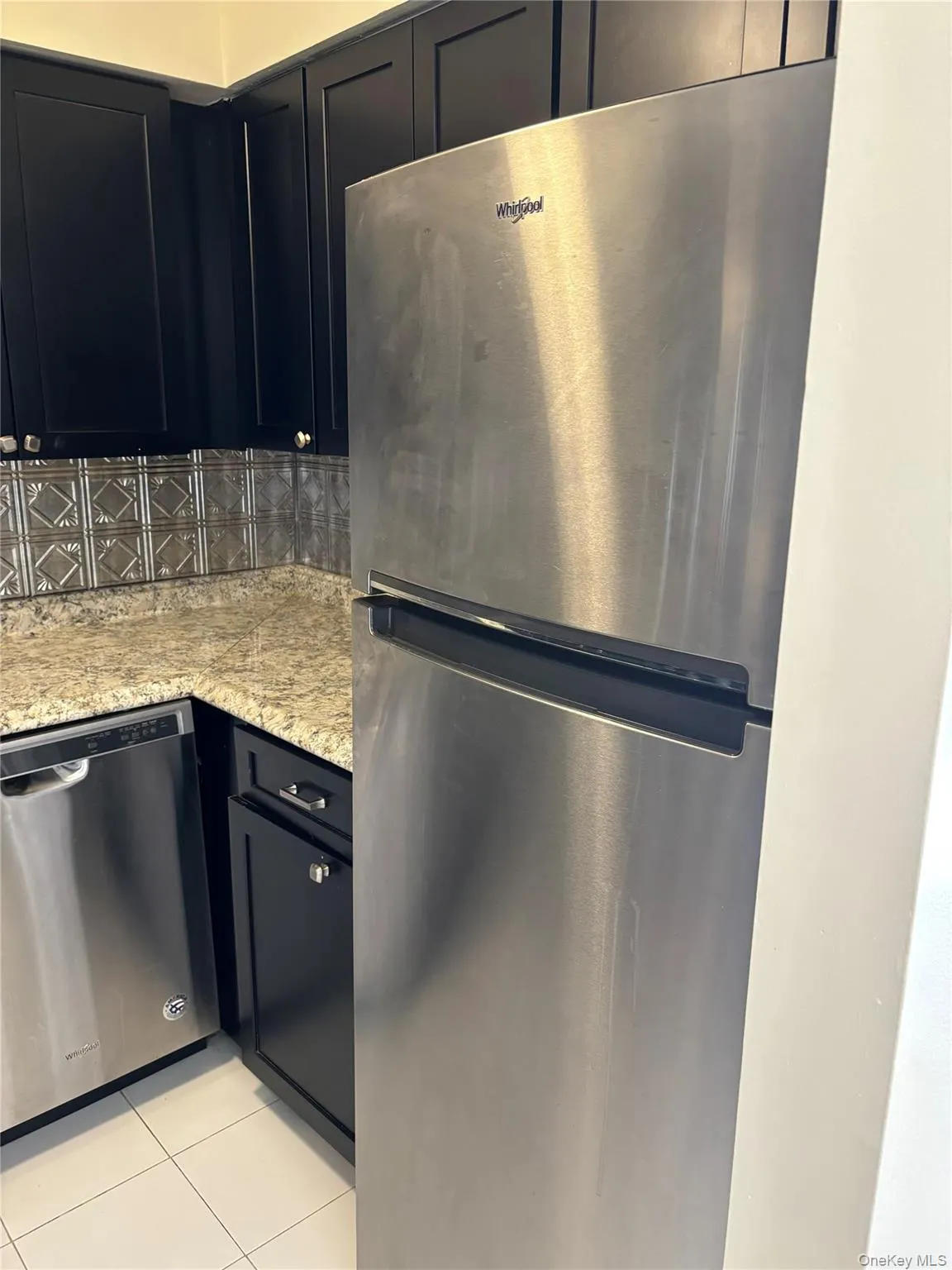 Kitchen with appliances with stainless steel finishes, light tile patterned flooring, light stone counters, and dark cabinetry Kitchen with appliances with stainless steel finishes, light tile patterned flooring, light stone counters, and dark cabinetry