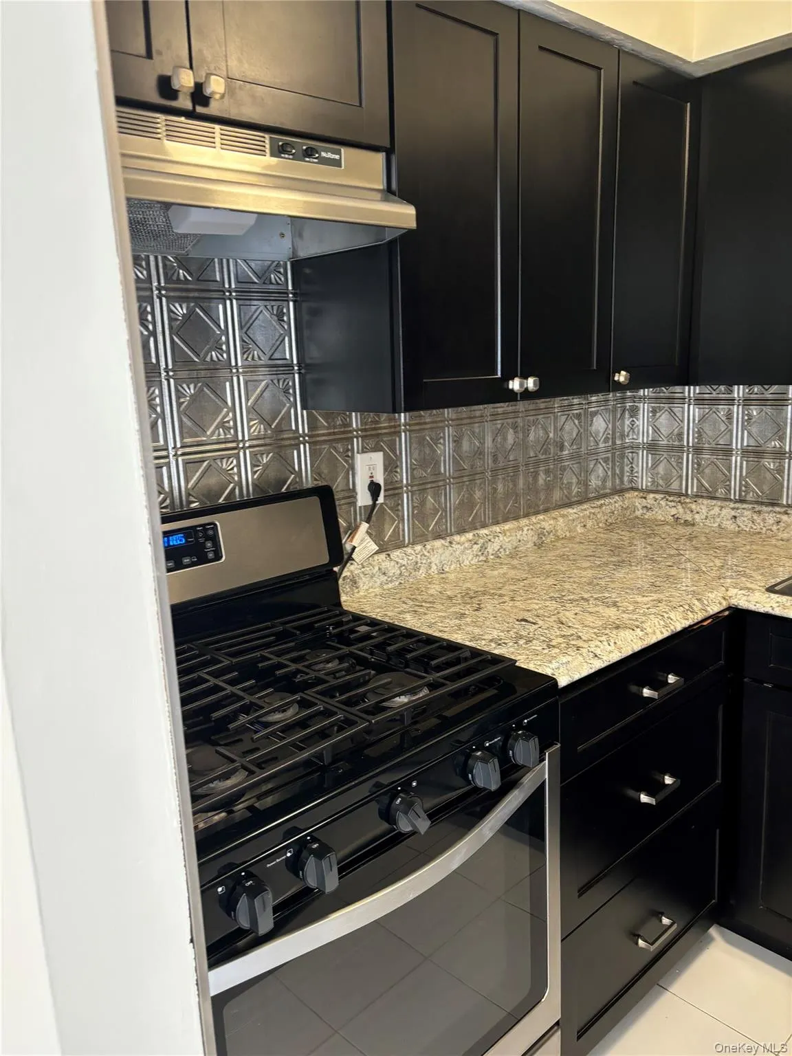 Kitchen featuring dark cabinetry, stainless steel range with gas stovetop, under cabinet range hood, light stone counters, and backsplash Kitchen featuring dark cabinetry, stainless steel range with gas stovetop, under cabinet range hood, light stone counters, and backsplash