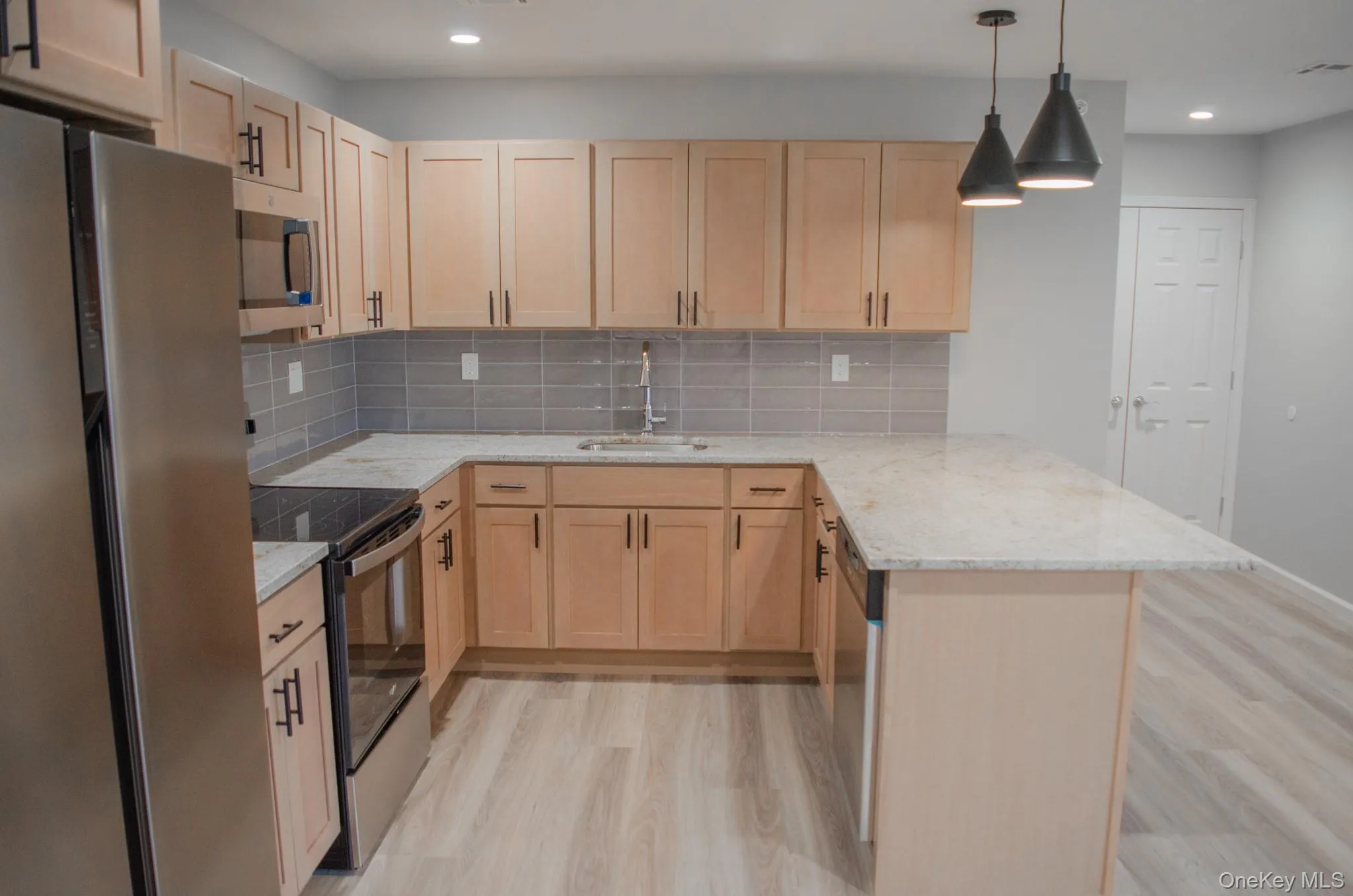 Kitchen with appliances with stainless steel finishes, a peninsula, light stone counters, pendant lighting, and light wood-style floors Kitchen with appliances with stainless steel finishes, a peninsula, light stone counters, pendant lighting, and light wood-style floors