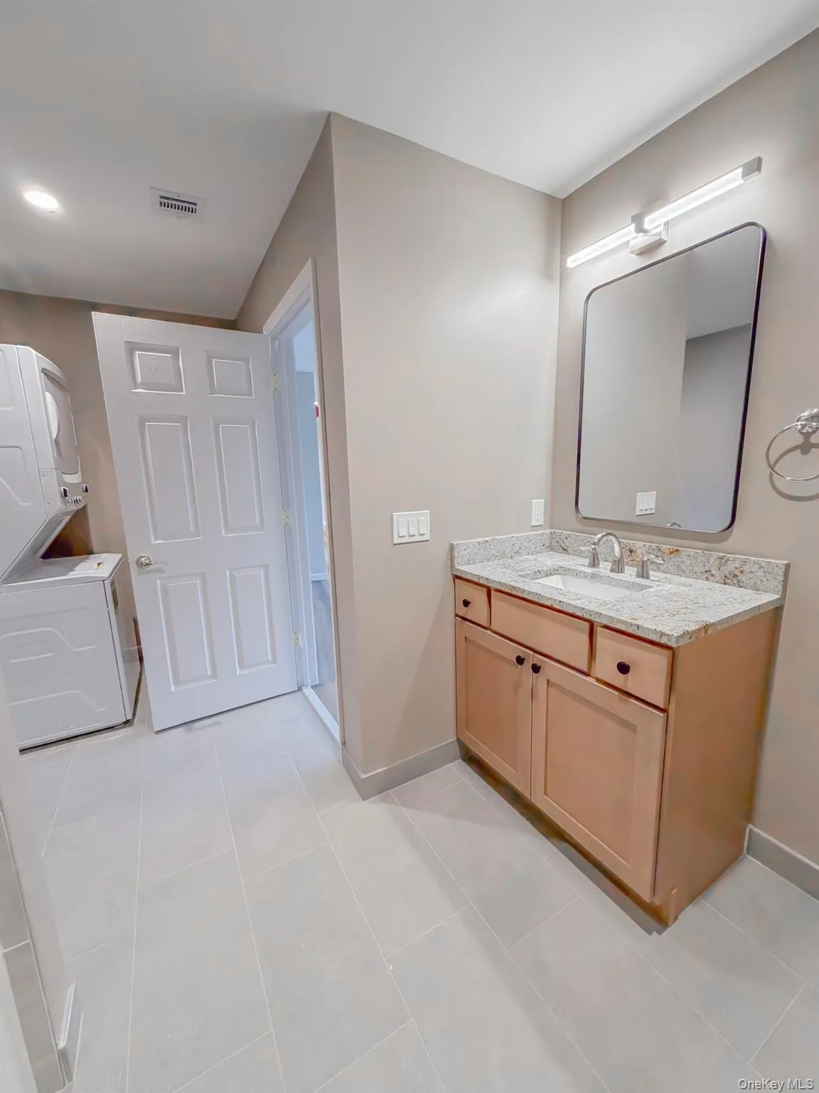 Bathroom featuring vanity, stacked washing machine and dryer, and light tile patterned flooring Bathroom featuring vanity, stacked washing machine and dryer, and light tile patterned flooring