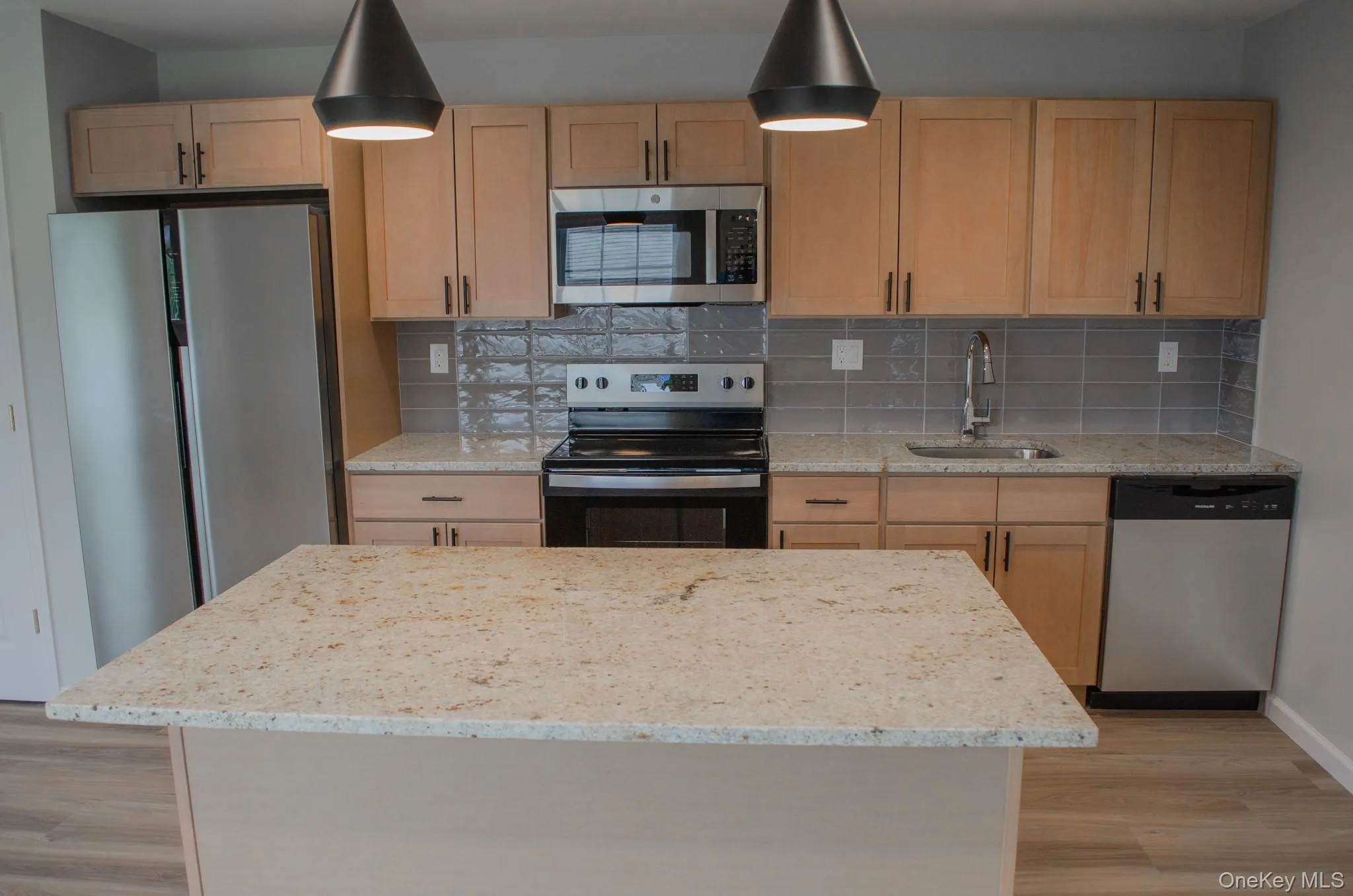 Kitchen with appliances with stainless steel finishes, light stone counters, light wood finished floors, and light brown cabinetry Kitchen with appliances with stainless steel finishes, light stone counters, light wood finished floors, and light brown cabinetry