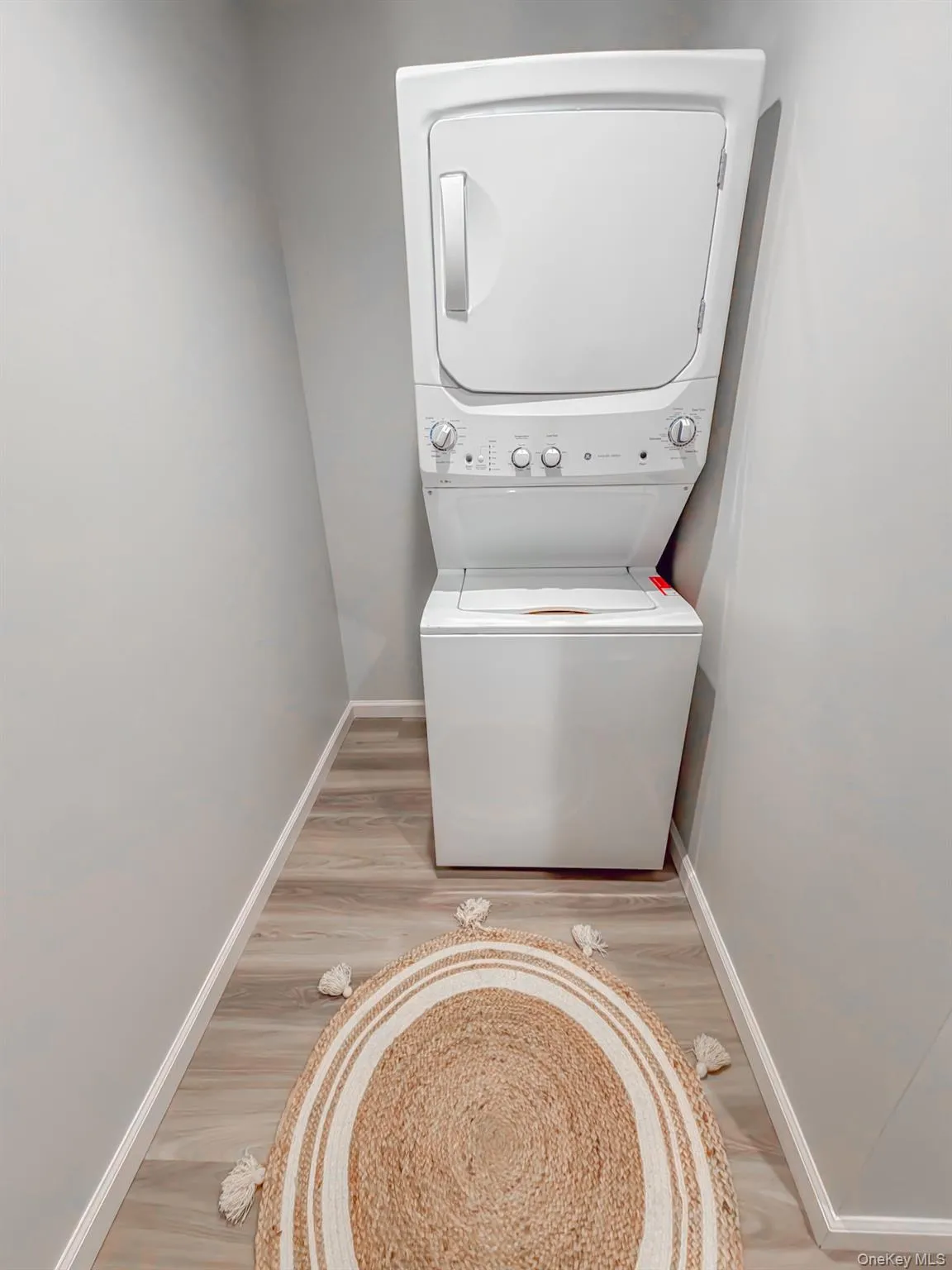 Laundry area featuring stacked washing machine and dryer and light wood-style floors Laundry area featuring stacked washing machine and dryer and light wood-style floors