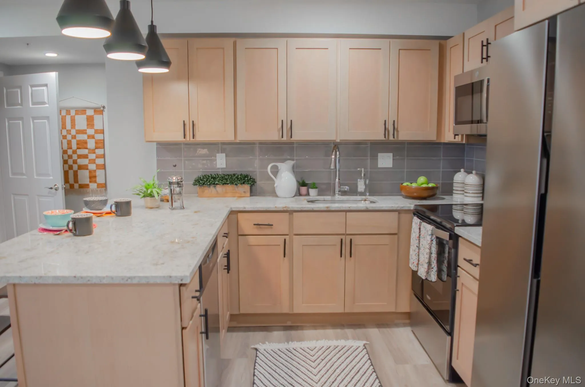 Kitchen with appliances with stainless steel finishes, light brown cabinetry, light stone countertops, and a peninsula Kitchen with appliances with stainless steel finishes, light brown cabinetry, light stone countertops, and a peninsula