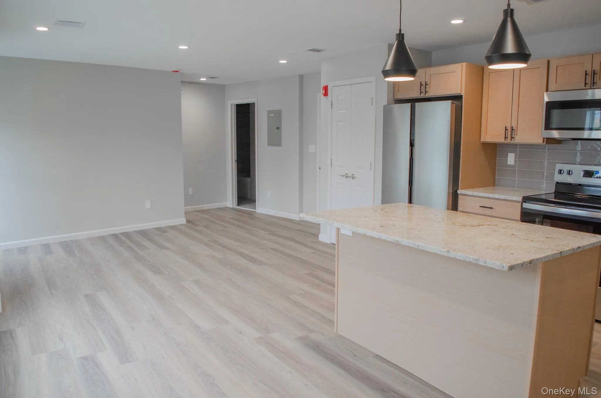 Kitchen with appliances with stainless steel finishes, a center island, light stone countertops, tasteful backsplash, and light brown cabinetry Kitchen with appliances with stainless steel finishes, a center island, light stone countertops, tasteful backsplash, and light brown cabinetry