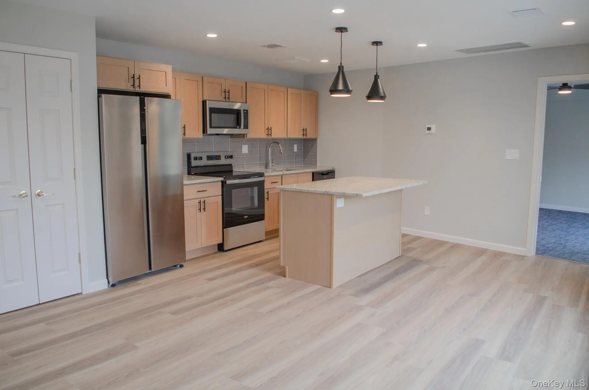 Kitchen featuring light brown cabinets, stainless steel appliances, decorative light fixtures, tasteful backsplash, and a kitchen island Kitchen featuring light brown cabinets, stainless steel appliances, decorative light fixtures, tasteful backsplash, and a kitchen island