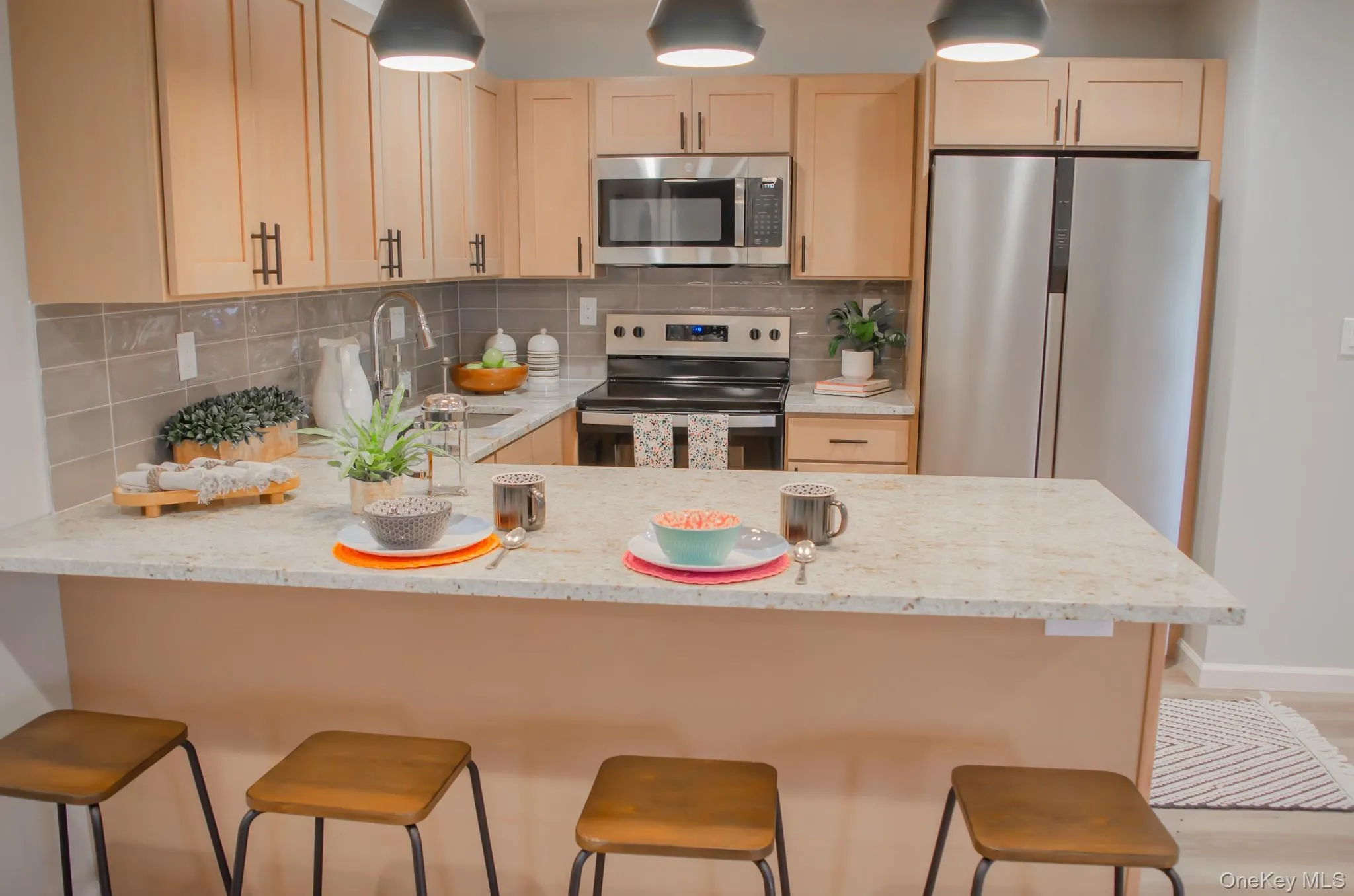 Kitchen featuring stainless steel appliances, light stone countertops, a peninsula, tasteful backsplash, and hanging light fixtures Kitchen featuring stainless steel appliances, light stone countertops, a peninsula, tasteful backsplash, and hanging light fixtures