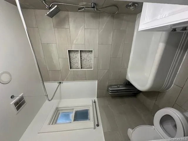Bathroom with bathtub / shower combination, radiator heating unit, tile walls, tile patterned flooring, and vanity Bathroom with bathtub / shower combination, radiator heating unit, tile walls, tile patterned flooring, and vanity