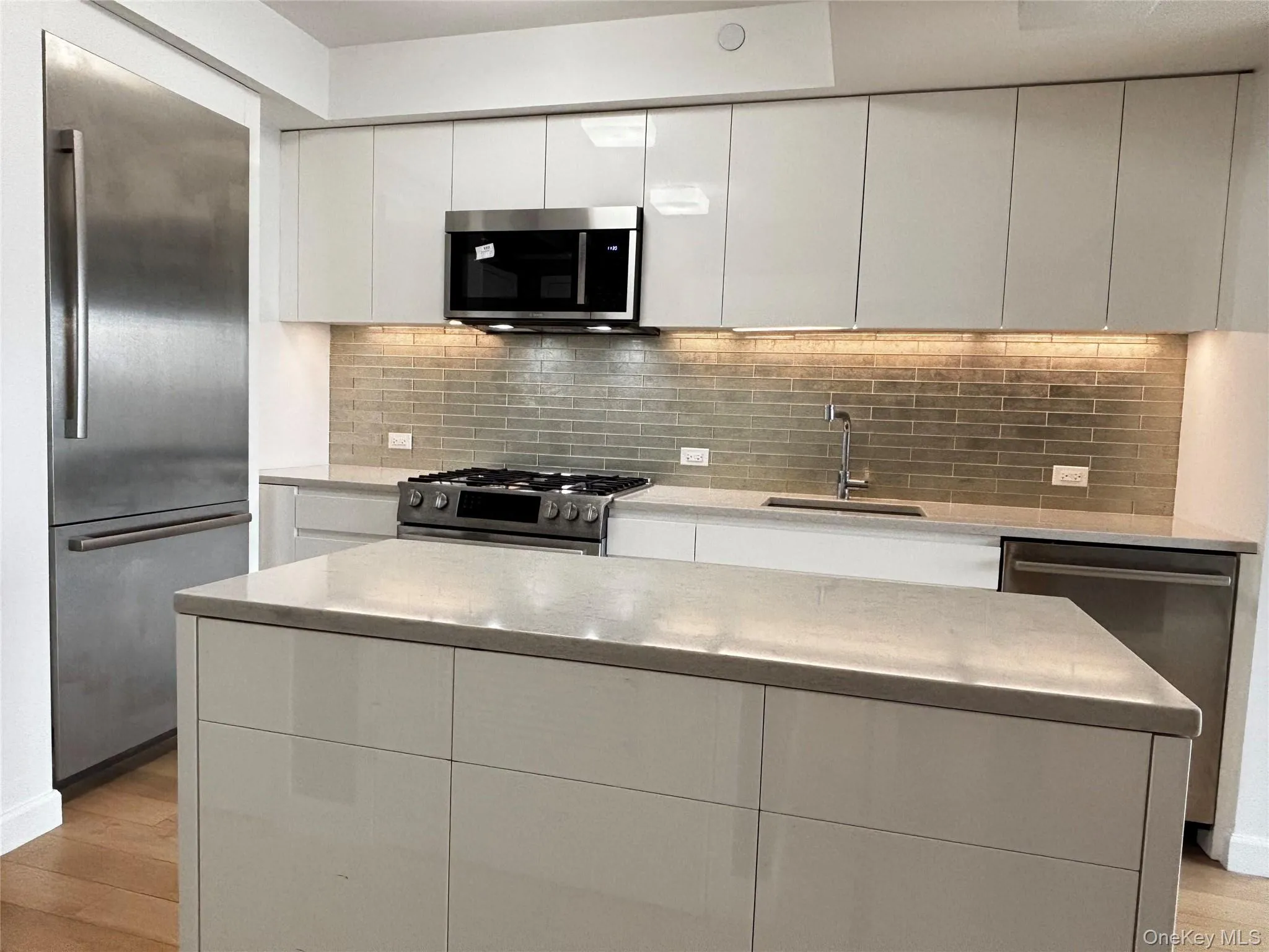 Kitchen with appliances with stainless steel finishes, modern cabinets, white cabinetry, and light wood-style floors Kitchen with appliances with stainless steel finishes, modern cabinets, white cabinetry, and light wood-style floors