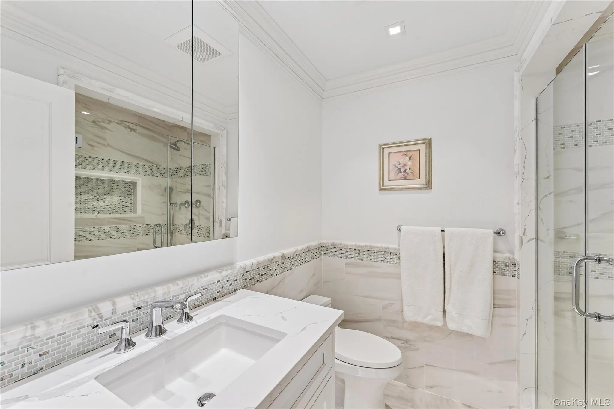 Full bathroom featuring crown molding, vanity, a marble finish shower, wainscoting, and tile walls. Full bathroom featuring crown molding, vanity, a marble finish shower, wainscoting, and tile walls.