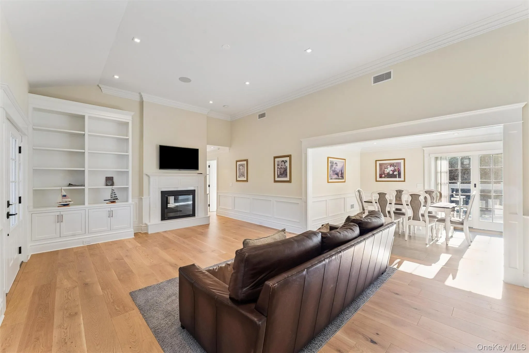Living room with a wainscoted walls, light wood flooring, and a glass covered fireplace. Living room with a wainscoted walls, light wood flooring, and a glass covered fireplace.