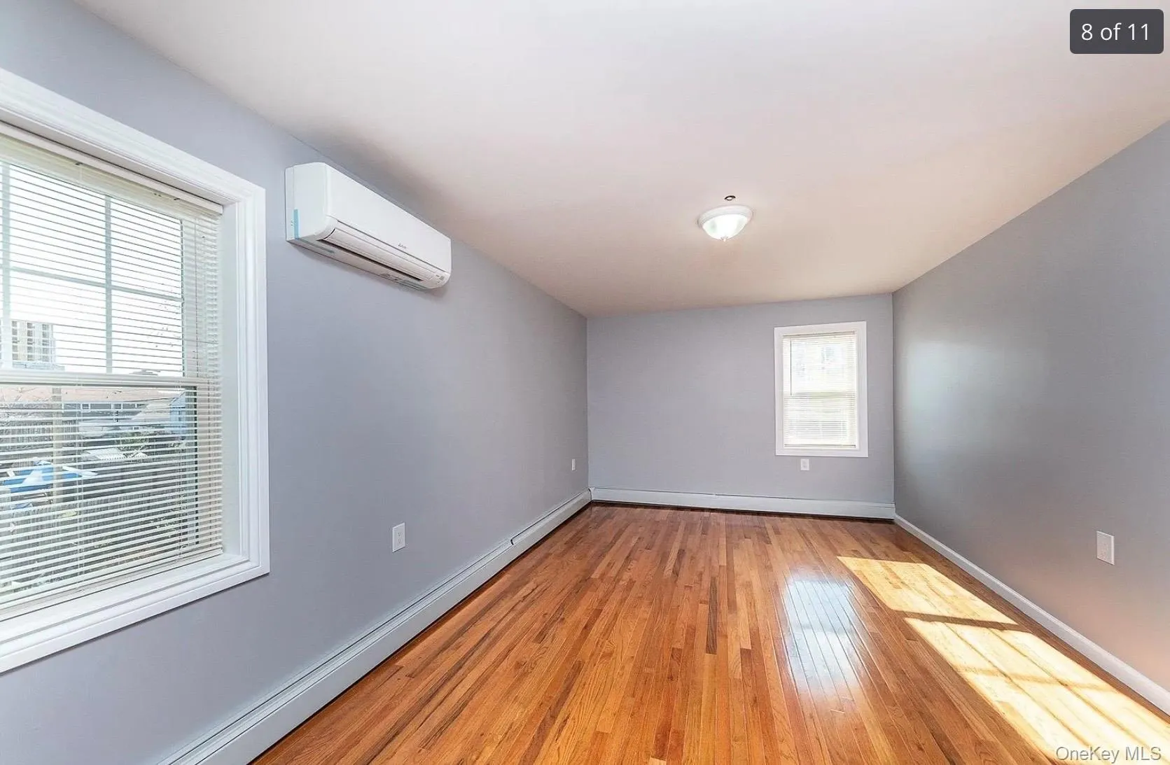Unfurnished room featuring baseboard heating, a wall mounted air conditioner, and light wood finished floors Unfurnished room featuring baseboard heating, a wall mounted air conditioner, and light wood finished floors