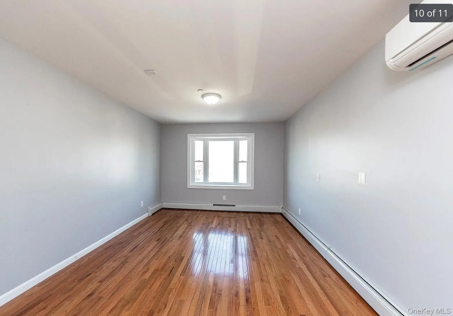 Unfurnished room featuring a baseboard radiator, a wall mounted AC, and wood finished floors Unfurnished room featuring a baseboard radiator, a wall mounted AC, and wood finished floors