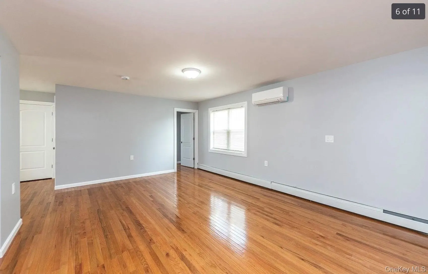 Unfurnished room with baseboard heating, light wood finished floors, and a wall mounted air conditioner Unfurnished room with baseboard heating, light wood finished floors, and a wall mounted air conditioner