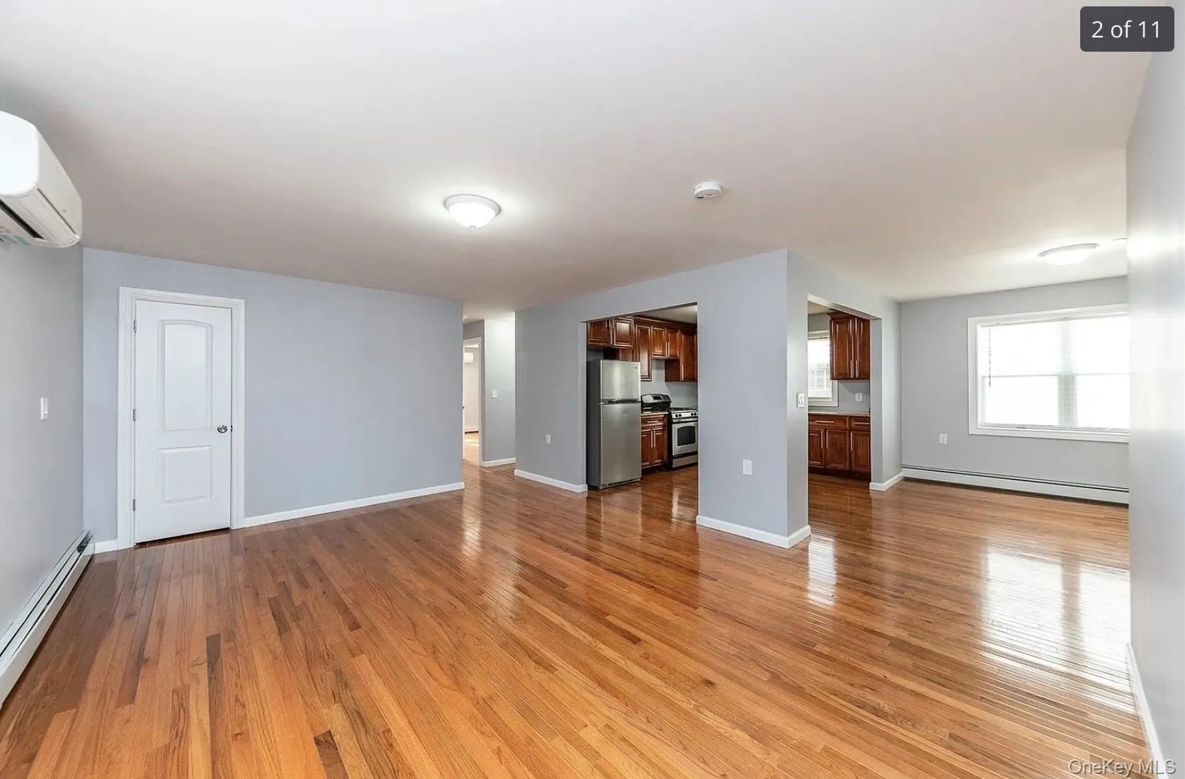 Unfurnished living room featuring a baseboard radiator, a baseboard heating unit, light wood-style floors, and a wall mounted AC Unfurnished living room featuring a baseboard radiator, a baseboard heating unit, light wood-style floors, and a wall mounted AC