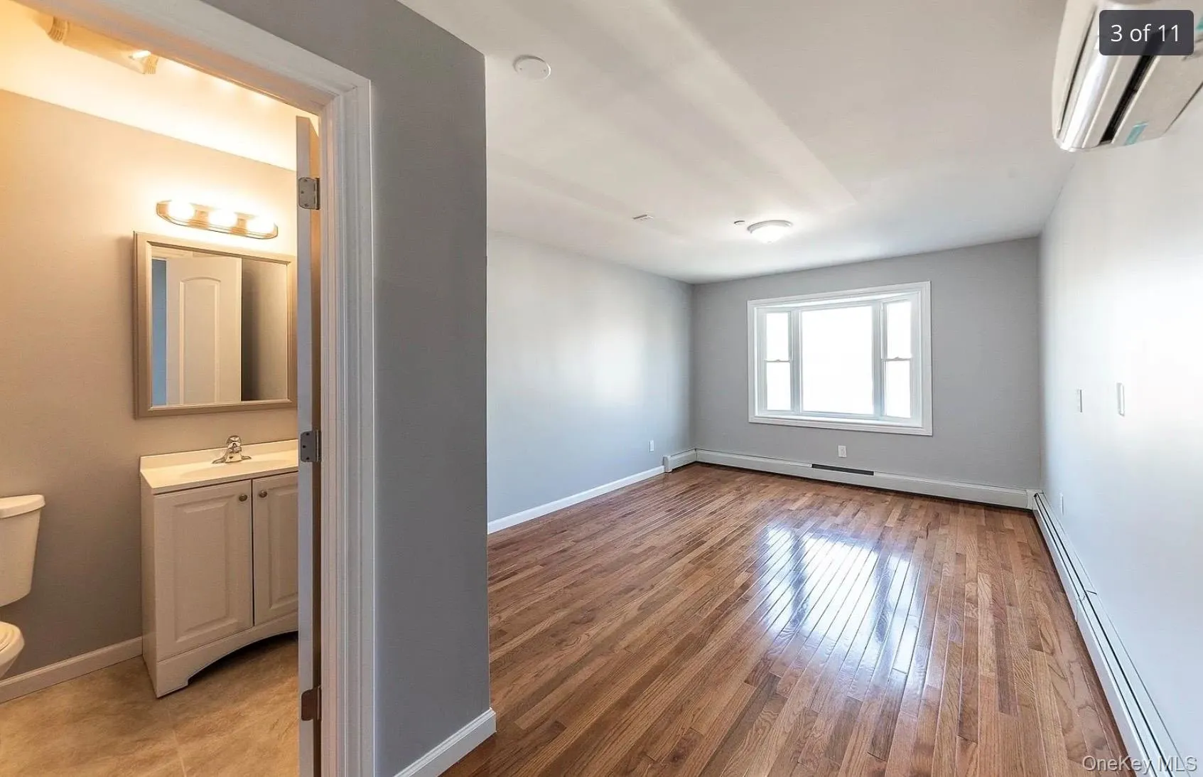 Empty room featuring a baseboard heating unit, an AC wall unit, and light wood-style floors Empty room featuring a baseboard heating unit, an AC wall unit, and light wood-style floors
