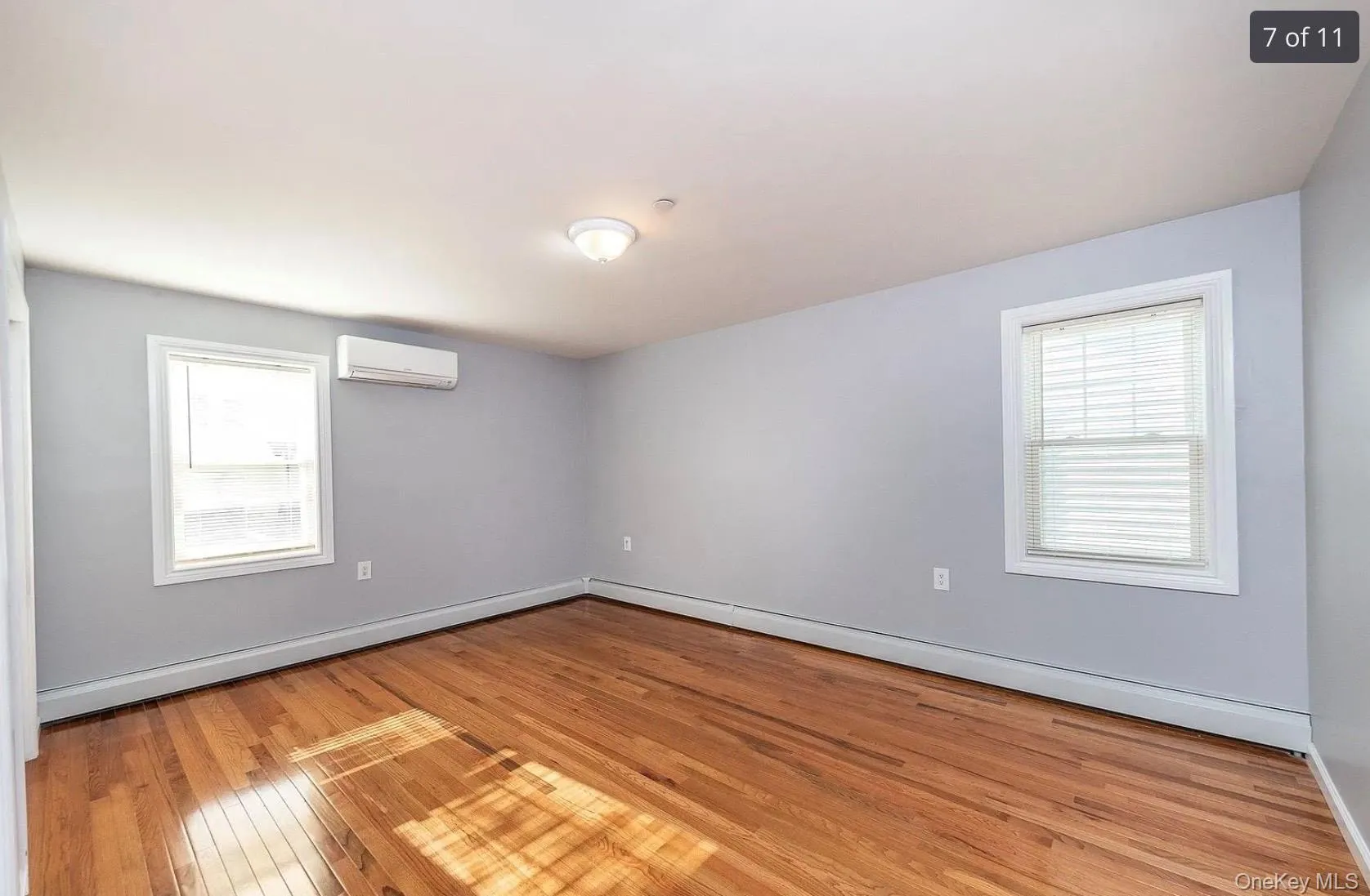 Unfurnished room featuring baseboard heating, light wood-style flooring, and a wall unit AC Unfurnished room featuring baseboard heating, light wood-style flooring, and a wall unit AC