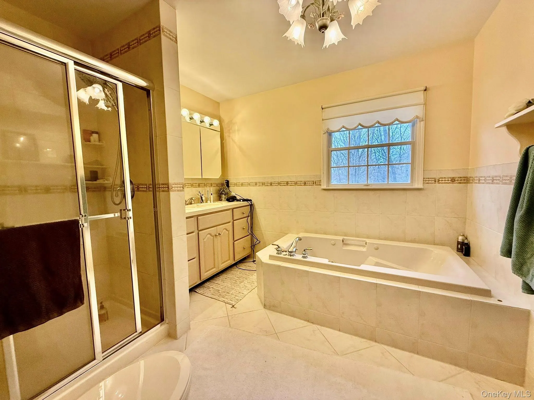 Full bathroom with vanity, a bath, tile walls, wainscoting, and light tile patterned flooring Full bathroom with vanity, a bath, tile walls, wainscoting, and light tile patterned flooring