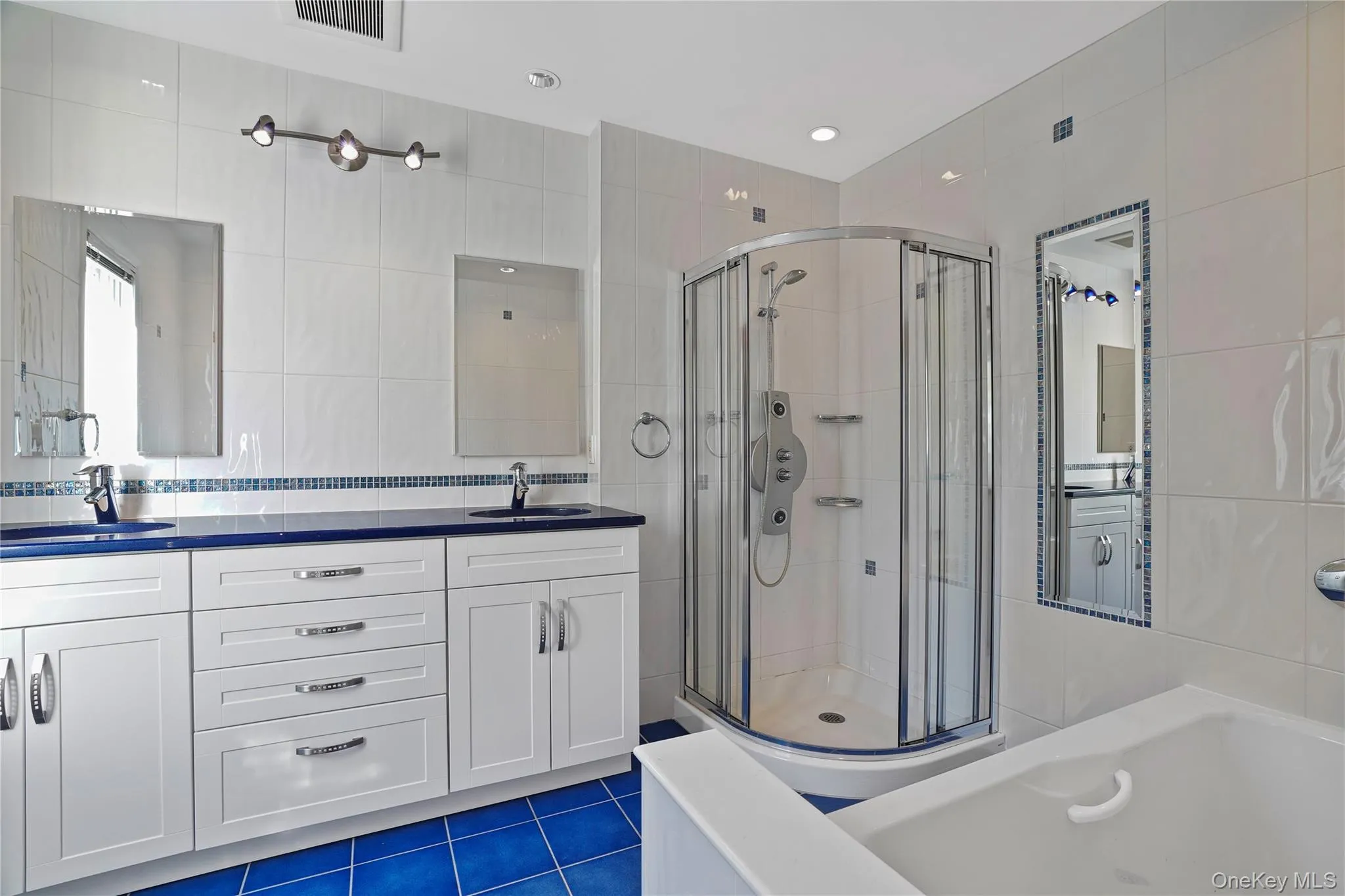 Full bathroom featuring tile walls, a garden tub, double vanity, dark tile patterned floors, and a shower stall Full bathroom featuring tile walls, a garden tub, double vanity, dark tile patterned floors, and a shower stall